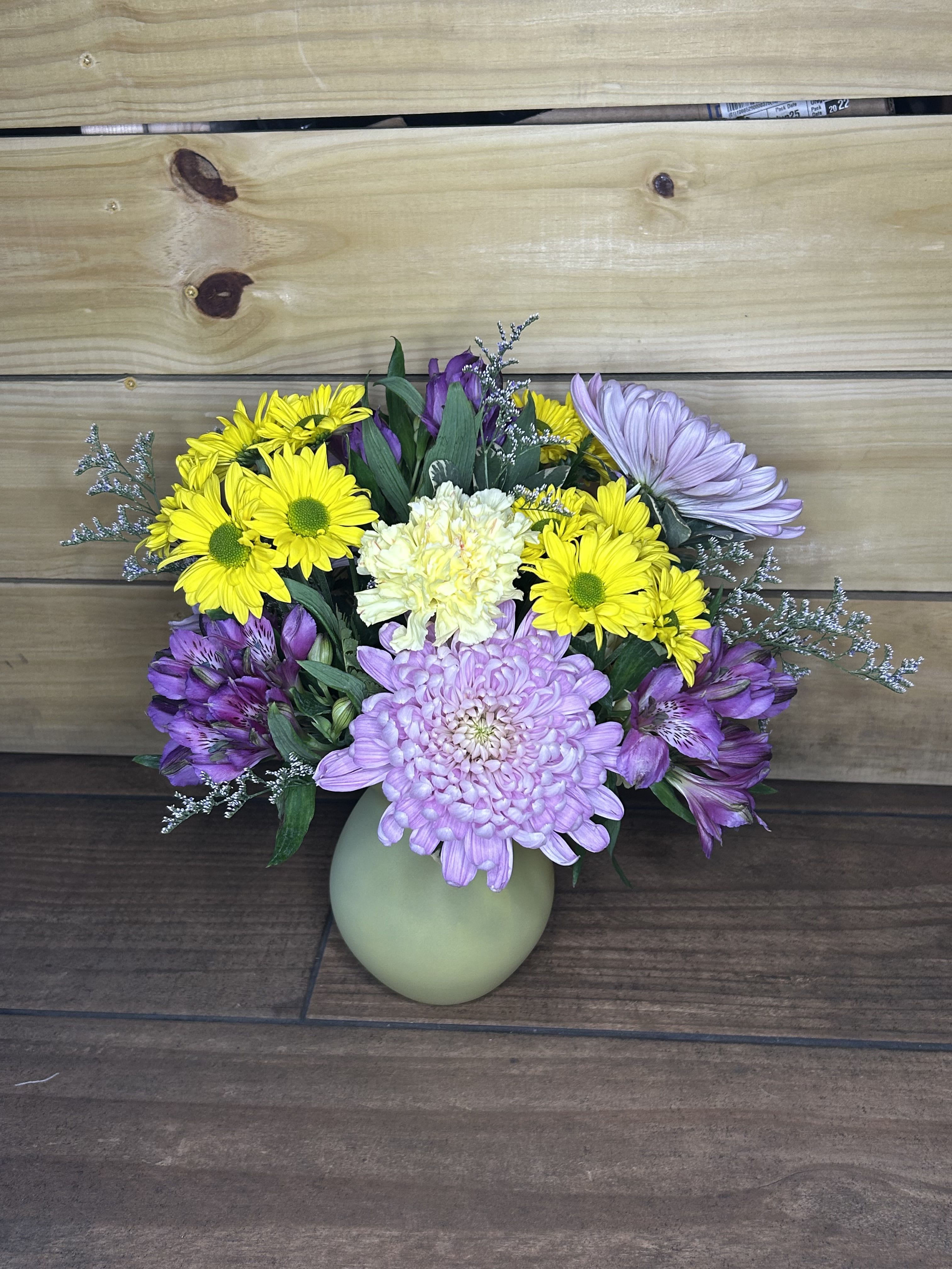 Golden Meadow Bloom - Bright and cheerful with a soft garden touch, Golden Meadow Bloom brings together sunny yellow daisies, delicate lavender mums, creamy carnations, and purple alstroemeria. Designed in a soft green glass vase and accented with airy filler and lush greenery, this arrangement has a fresh, meadow-inspired feel. Its vibrant yellow and gentle lavender tones create a perfect balance of warmth and calm—making it a lovely gift for birthdays, get-well wishes, thank-yous, or simply brightening someone’s day.