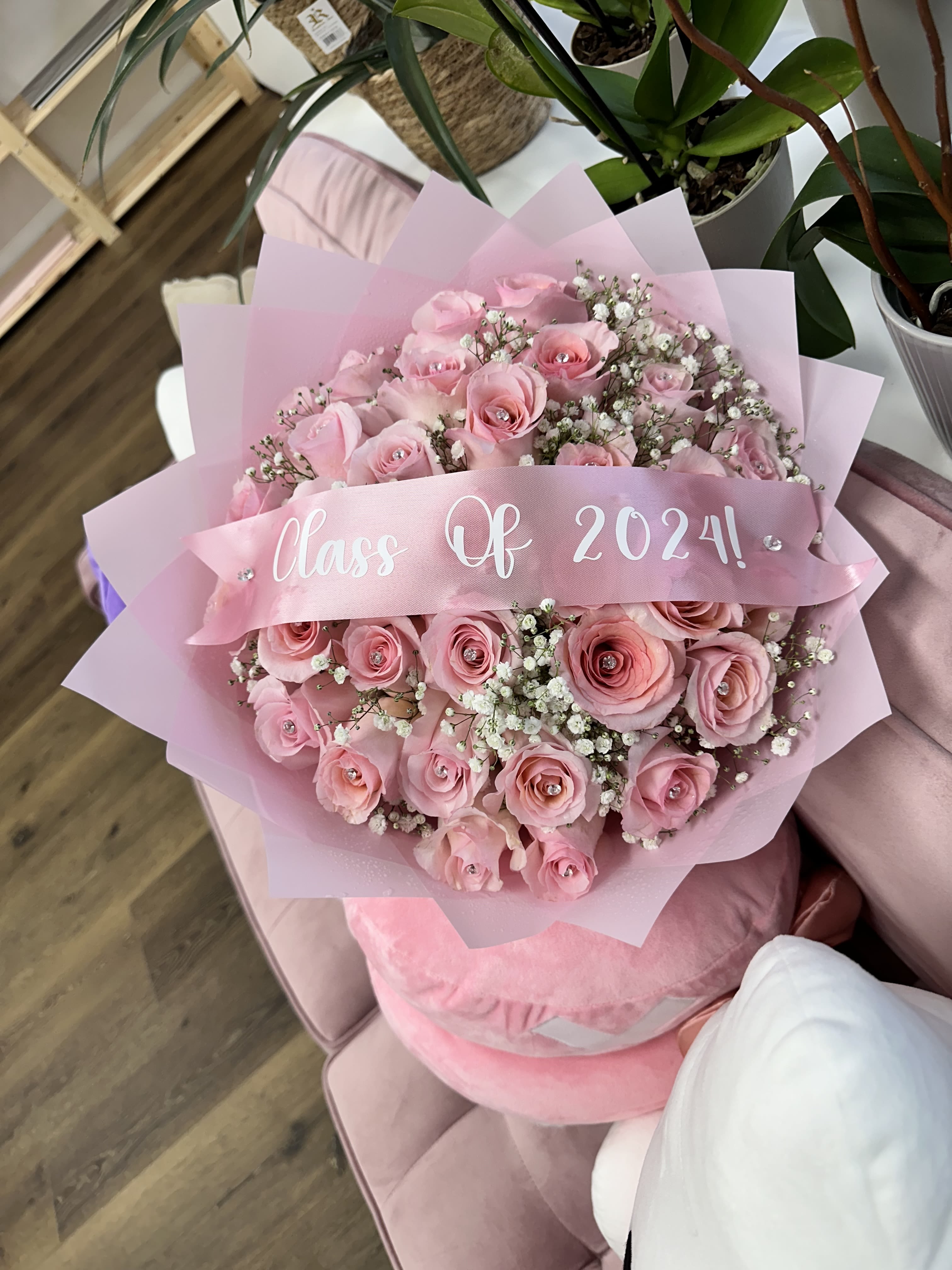 Enchanter Rose Delight Bouquet - Experience the timeless charm of our Enchanted Rose Delight bouquet. Featuring 25 stunning pink roses adorned with sparkling diamonds at their centers, this arrangement is a true vision of elegance. Each rose is gracefully nestled among delicate baby’s breath and wrapped in elegant pink paper. *PLEASE CALL THE STORE TO CHANGE THE LETTERING ON THE BANNER*