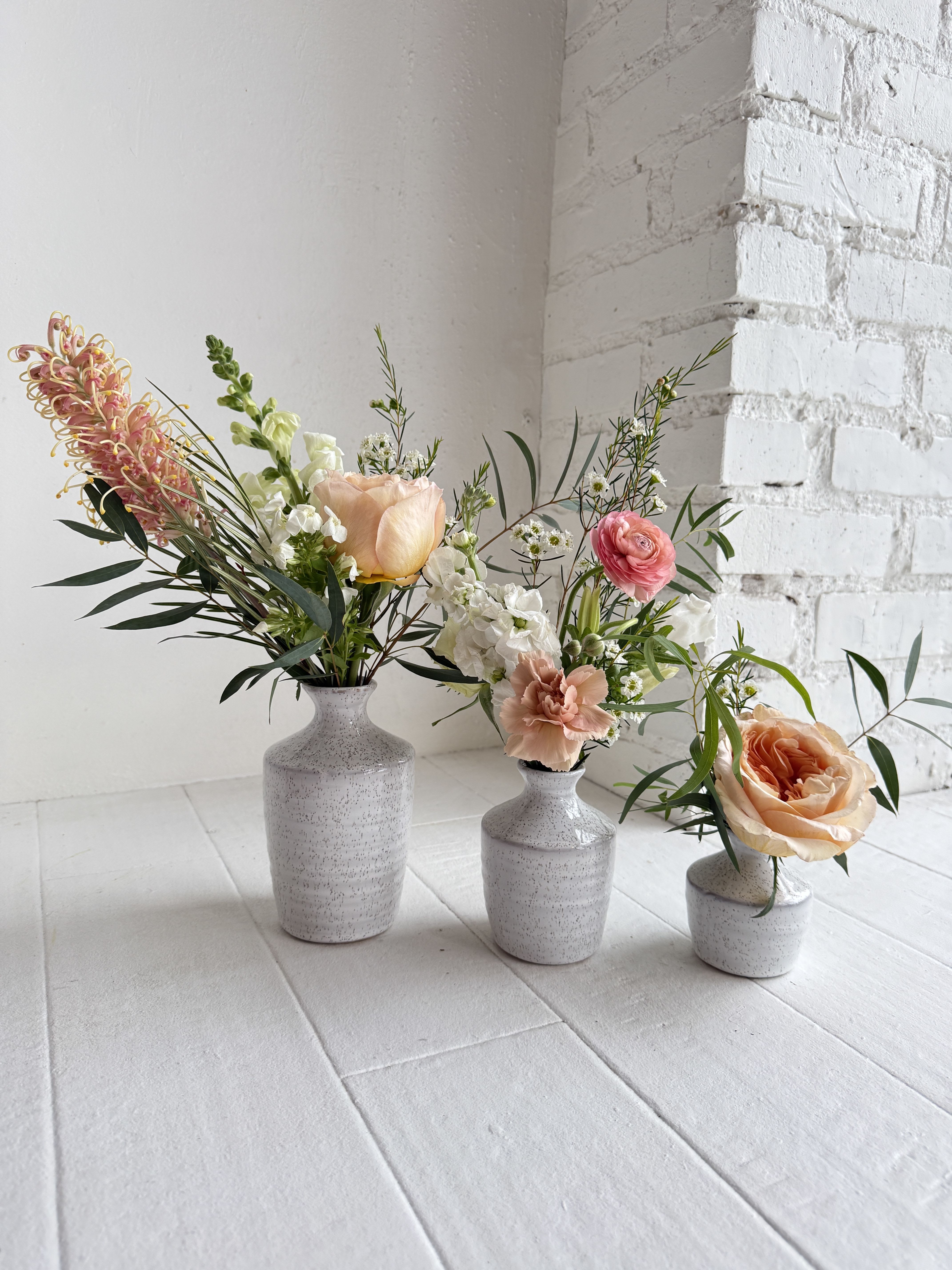 Eva - An eclectic mix of mostly peach flowers, with some white flowers in a set of three vases.