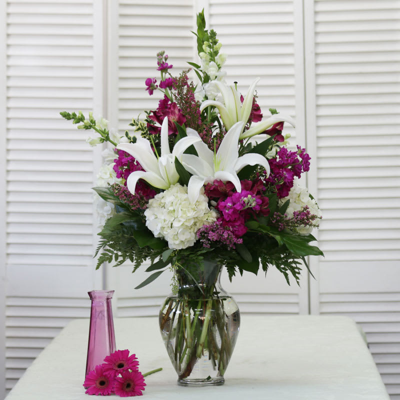 Fancy and Fuchsia  - This Stunning Vase arrangement includes White Lilies as the focal point and is adorned with White Snapdragons and Hydrangea, Fuscia Stock &amp; Alstromeria.