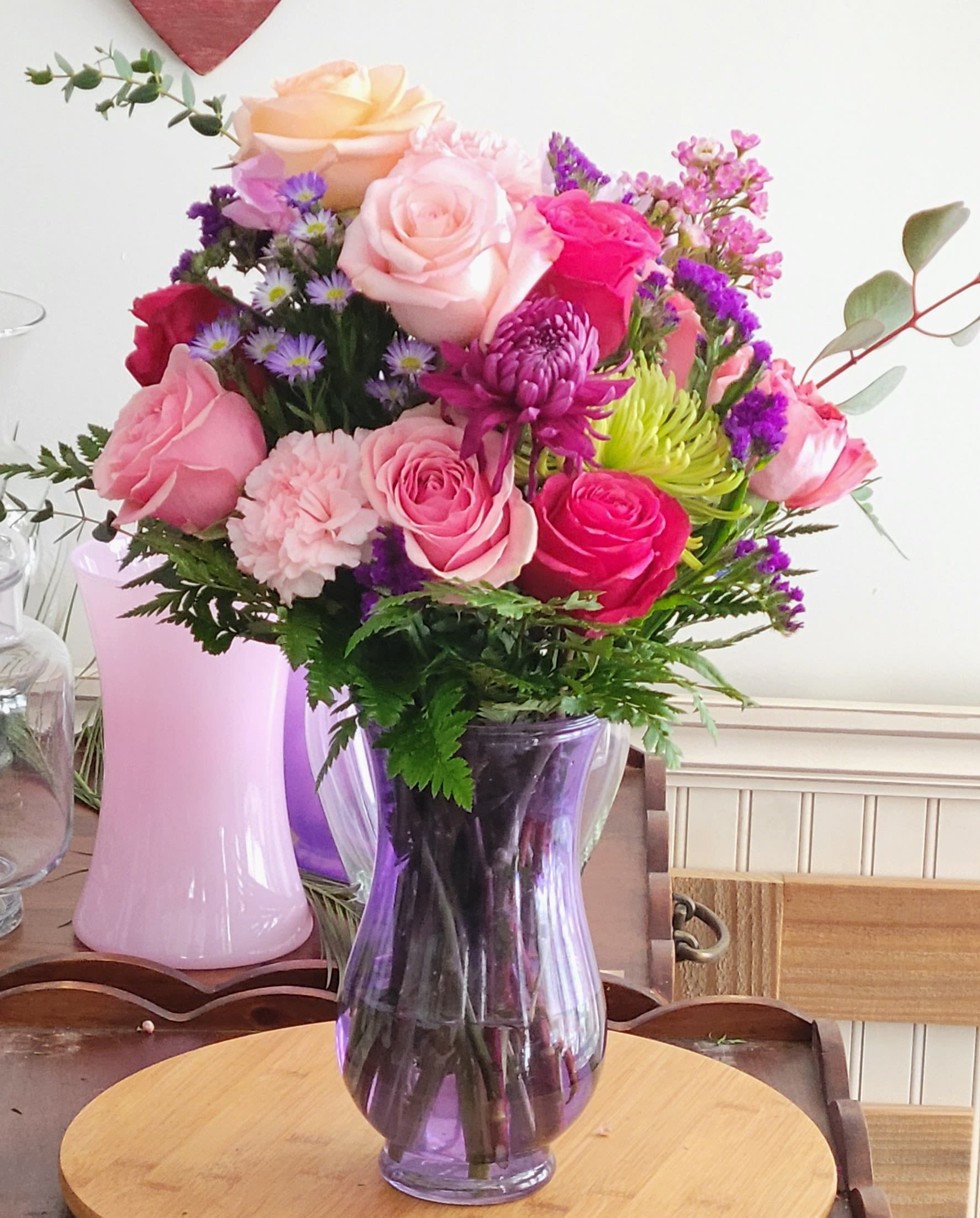 Indy's favorite by Dixie's Flowers - Reminder of your smile and gleam in your eyes designed by Indy Rae.  Filled with roses, mums, carnations and aster.  A vibrant, garden-style arrangement bursting with color and texture. The bouquet features a lively mix of warm soft pinks, purples, and lush greens, arranged in a natural, flowing style. With a balanced blend of bold blooms and delicate filler accents, this design brings a cheerful, organic elegance—perfect for brightening any space or celebrating a special moment.