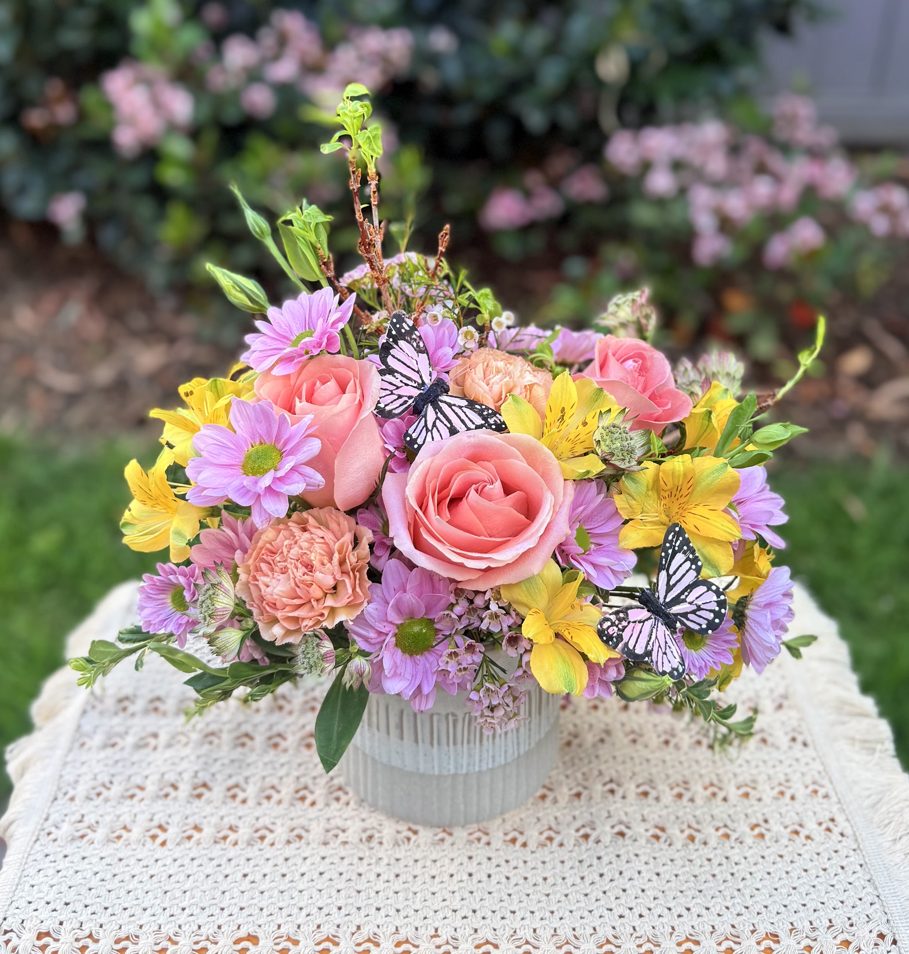 Spring Floral Arrangement - Spring at home with this gorgeous spring floral arrangement crafted with beautiful seasonal blooms: Ecuadorian roses, fancy carnations, elegant alstroemerias, wax flowers, daisy pompoms, seasonal foliage, it’s accented with 2 soft pink butterflies. It includes a ceramic vase in soft neutral colors. Medium size 