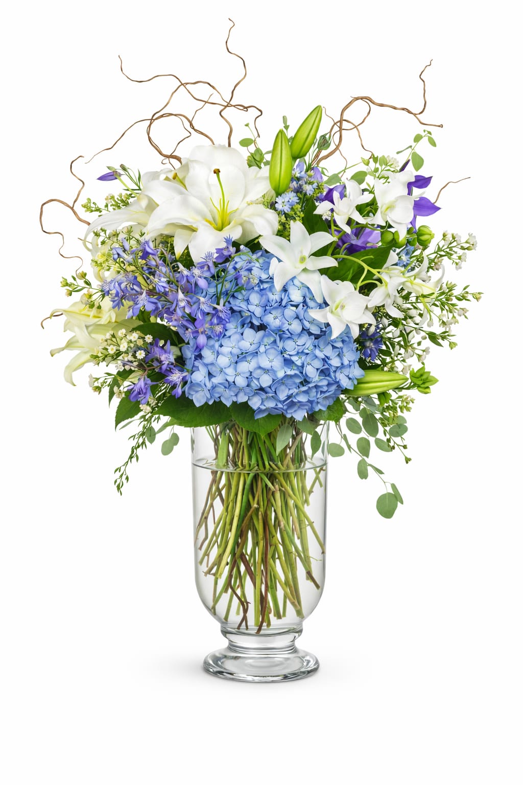 Tall arrangement of white lilies and blue hydrangeas with purple accents in a clear glass vase