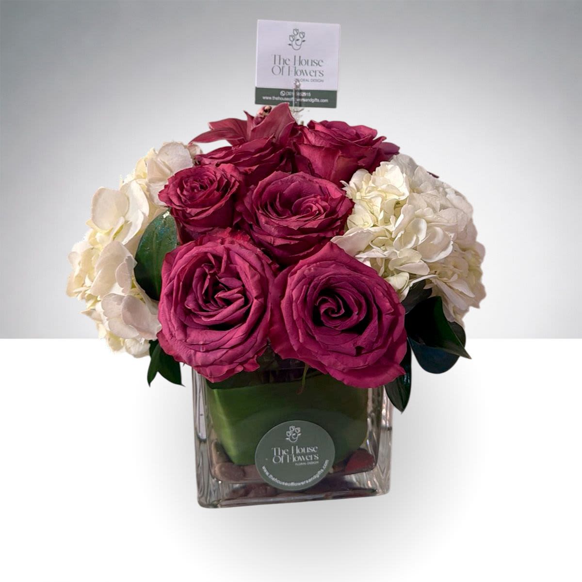 Ruby Garden Bloom by The House of Flowers - Ruby Garden Blooms is a sophisticated floral arrangement that blends rich color with timeless elegance. This design features vibrant ruby-toned roses beautifully paired with soft white hydrangea, creating a striking contrast that feels both luxurious and refined.  Arranged in a modern glass vase with decorative river stones and lush greenery, this arrangement brings a fresh garden-inspired style to any space.  Perfect for celebrating special moments, sending love, or adding a touch of elegance to a home or office.