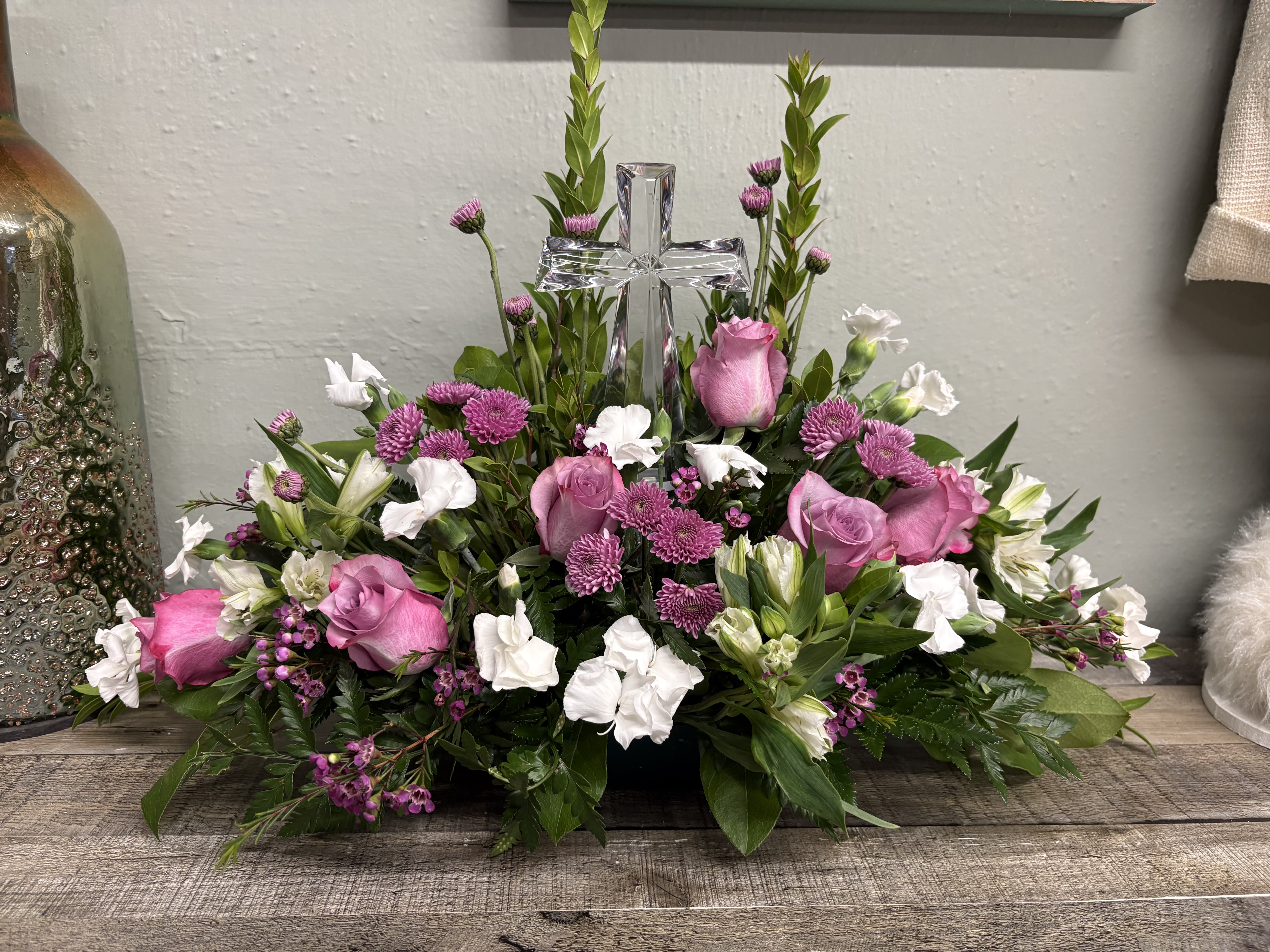 Teleflora’s Poised with Love - Soft and serene, this artistic array of cream and lavender blooms around a radiant crystal cross keepsake is a heartfelt expression of love.. This beautiful piece includes shades of lavenders and purples. You may request other colors, just call and we can help you change the flower section . Delivered with Teleflora's Small Crystal Cross. Orientation: One-Sided