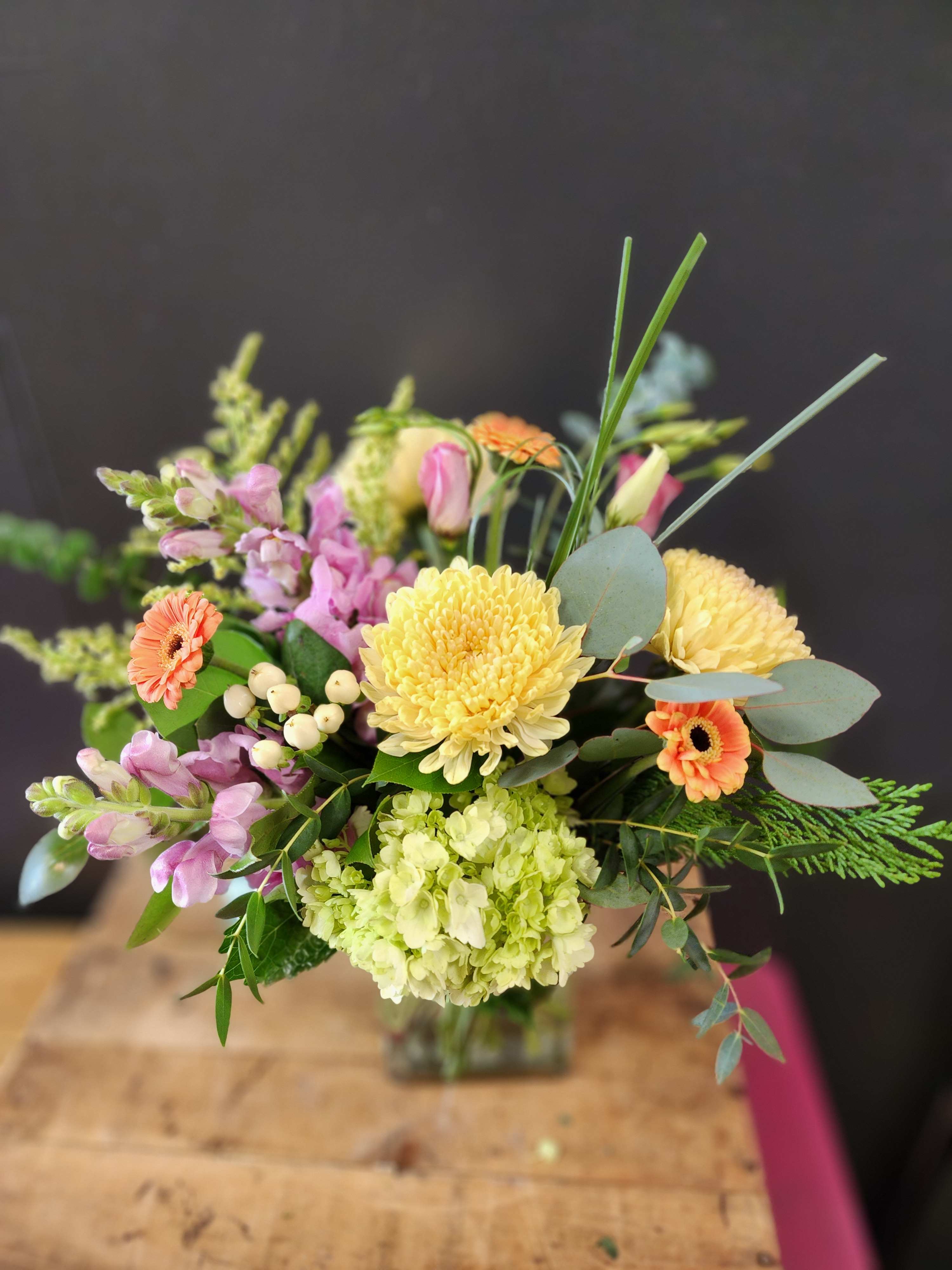 Hints of Spring - This bouquet is designed one sided with cremones, snap dragons, lisianthus, hydrangea, hypericum, and micro gerbera daisies.  *Some stages of flower life may vary. (Example: Lilies may be more open than imaged.) Flower shortages and product availability means that some substitutions will apply. Value will always be filled. This bouquet might include eucalyptus amongst the greenery. It may be toxic to pets including but not limited to Cats and Dogs if digested.