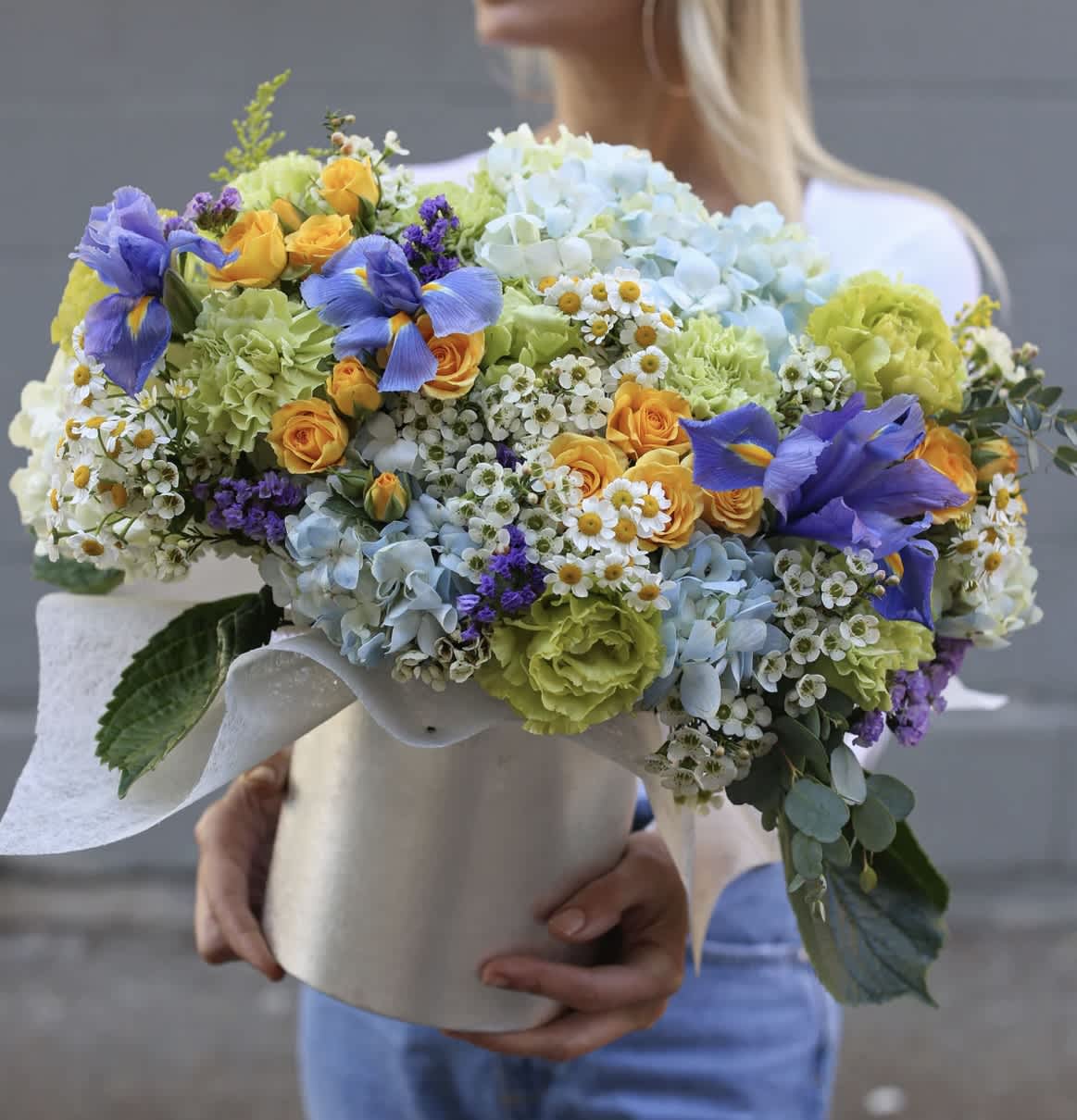 Large bouquet of blue, yellow, and green flowers wrapped in white paper