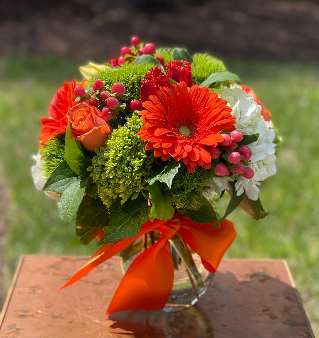 Orangina - Orangina – Vibrant Orange &amp; Green Floral Arrangement | Wilmington, Delaware Local Florist  Brighten any celebration with Orangina, a bold and cheerful floral arrangement created by your trusted Wilmington, Delaware florist. This eye-catching bouquet features fresh green hydrangea, soft white hydrangea, coral hypericum berries, vibrant orange roses, and striking orange Gerber daisies. Expertly arranged in a clear glass vase and finished with a bright orange satin ribbon, this design adds a pop of color and joy to any space.  Perfect for birthdays, anniversaries, congratulations, or just because. Available for same-day flower delivery in Wilmington, DE and nearby areas. Choose our local flower shop for premium blooms and friendly, reliable service.  