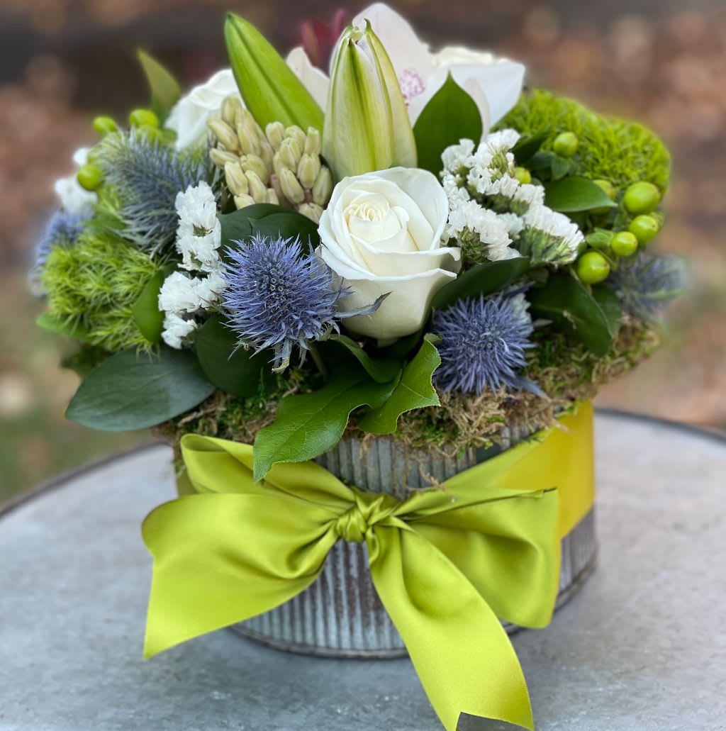 The Antoinette  - Elevate any occasion with our elegant Antoinette arrangement, exclusively designed by Petals Flowers and Fine Gifts — your premier local florist in Wilmington, Delaware. This sophisticated floral creation features lush green trichilium, graceful white lilies, classic white roses, striking blue thistle, and a stunning orchid. Each bloom is artfully arranged in a rustic corrugated metal container, finished with natural moss and tied with a charming green ribbon for a refined, garden-inspired look.  Perfect for anniversaries, sympathy gestures, housewarmings, or simply to add timeless beauty to your home, the Antoinette brings together texture, soft hues, and unique accents for an unforgettable floral display.  As a boutique florist in Wilmington, Delaware, we specialize in luxury, custom-designed flower arrangements crafted with exceptional attention to detail. We proudly offer same-day, tax-free delivery throughout Wilmington, Hockessin, Newark, Glen Mills, Chadds Ford, Kennett Square, and nearby communities — always backed by our satisfaction guarantee.  Why Choose Us?  * Locally owned and operated florist delivering throughout Wilmington and surrounding areas * Premium flowers and artistic, garden-style designs tailored to your needs * Personalized service with a commitment to quality and care Order the Antoinette today and let us deliver natural elegance and lasting impressions to your loved ones or special events in Wilmington, Delaware.