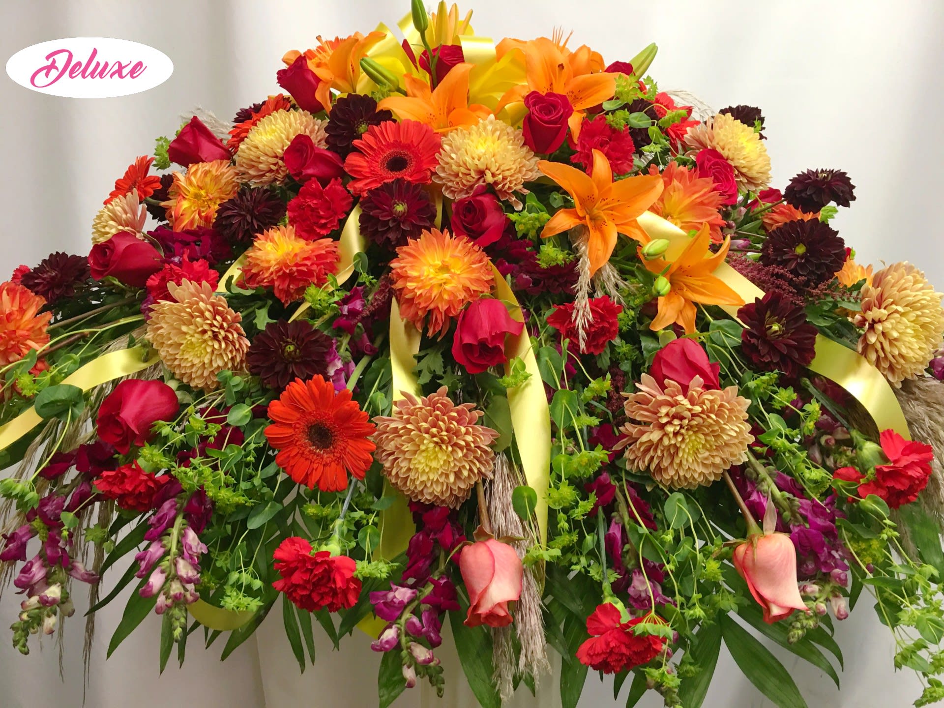 Sunset Autumn Casket Cover  - Sunset Autumn Wreath is a beautiful assortment of seasonal flowers that include ruby red roses, rust colored mums, deep burgundy snap dragons, bright orange lilies, bright red gerbera daisies and other seasonal flowers 