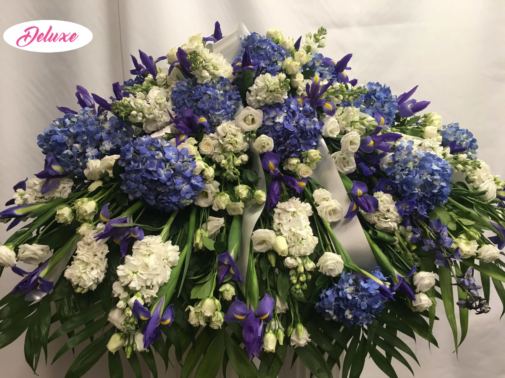 Beautiful in Blue Cover - This Casket cover is beautiful in blues &amp; whites. All Holland flowers make this piece elegant. Flowers include Hydrangea, Lilies, Stock, Delphinium &amp; other seasonal flowers 
