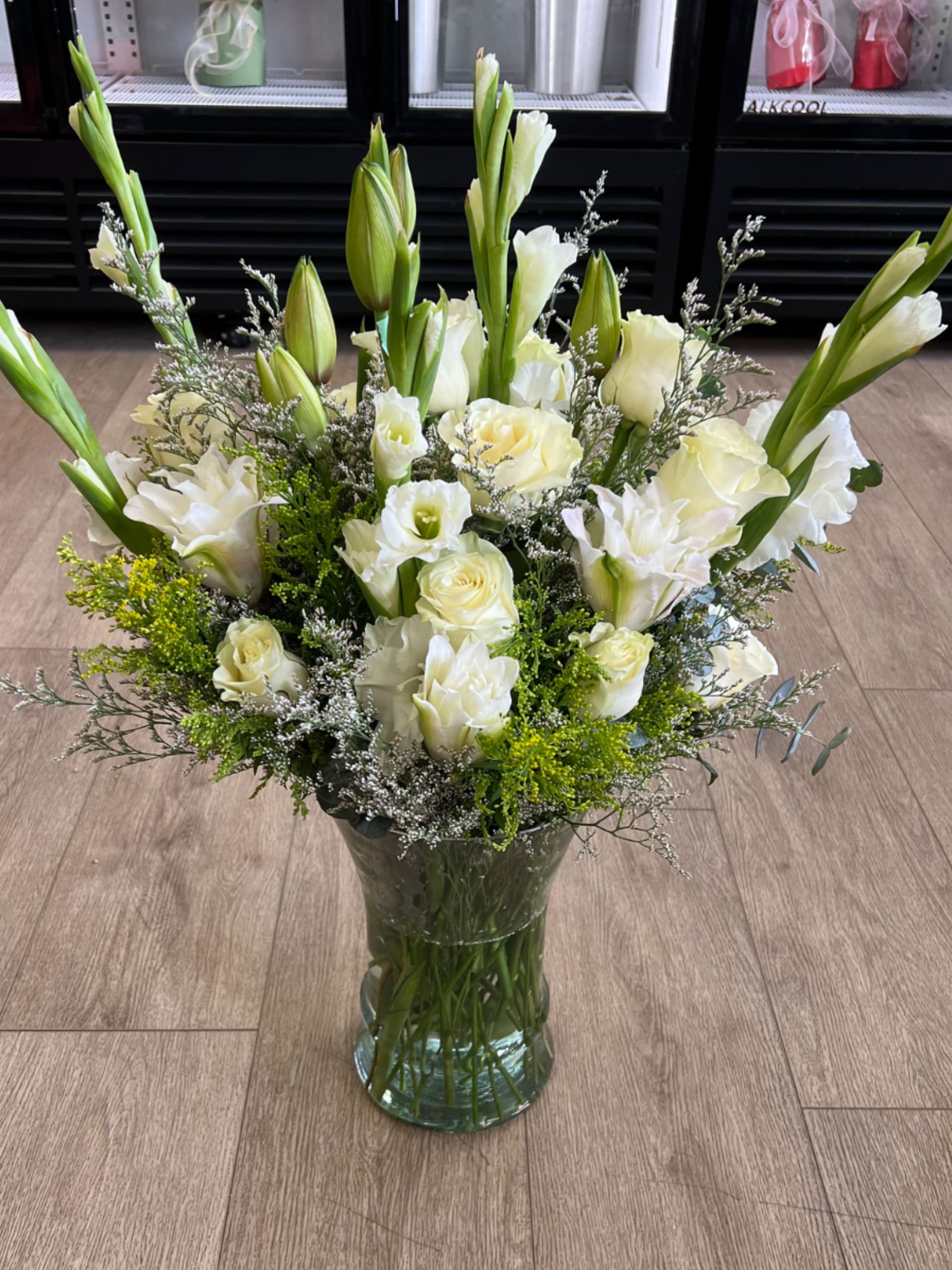 Extra Large sympathy arrangements in glass vase - A mix of white roses, lilies, and greenery, arranged with accents of eucalyptus and delicate filler flowers.
