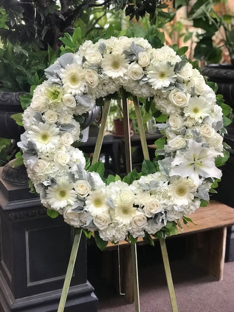 Circle of Life - A light and ethereal circular wreath. Designed in clean whites &amp; greens, accented with the soft texture and grey color of dusty miller. The size of the wreath foam is 18" with floral extending to about 20"-22" on an easel that ranges from 48"-56" in height.