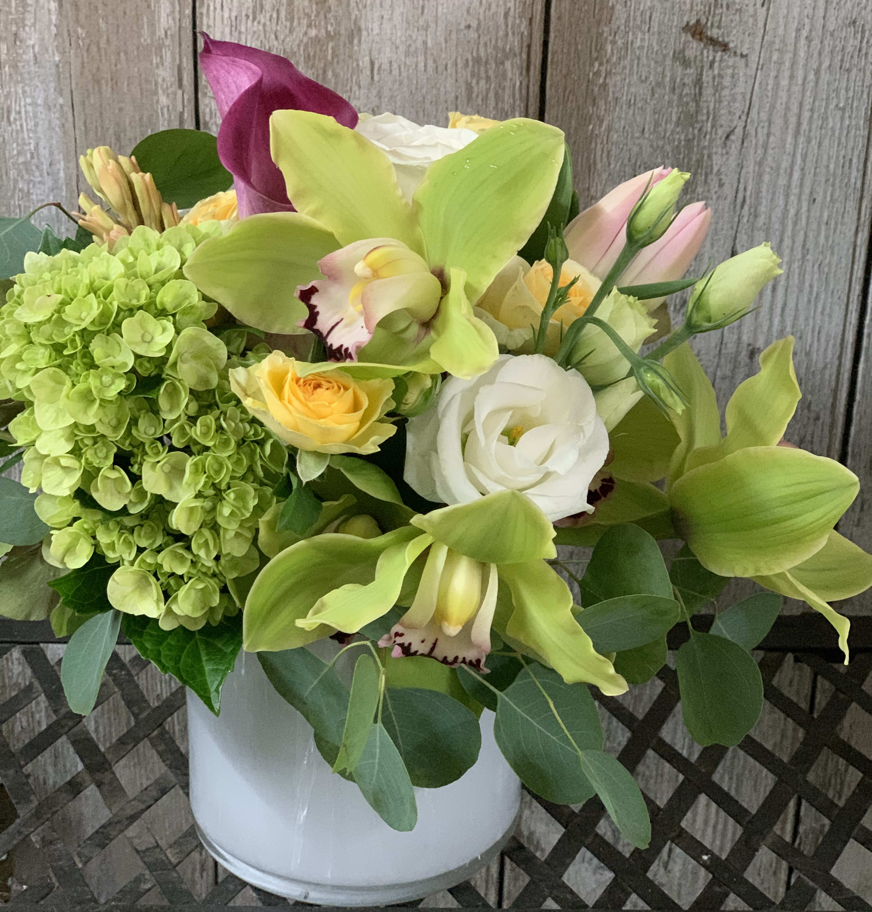 Pastel fusion - Green cymbidium, white roses, bandalero spray roses, pink calla lily, green hydrangea, hellebore dance together in a white cylinder 