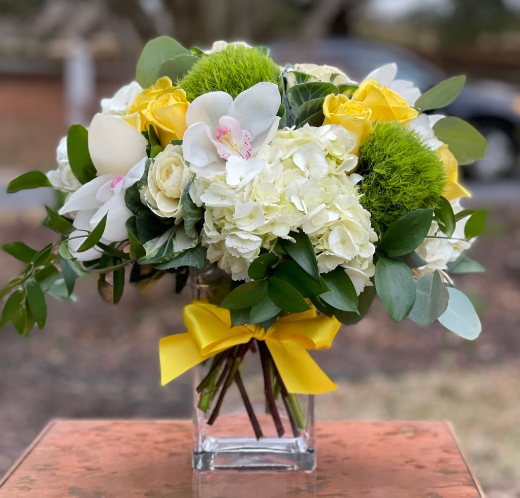 Lemon Verbena  - Lemon Verbena – Fresh Yellow &amp; White Floral Arrangement | Wilmington, Delaware Local Florist  Brighten any space with Lemon Verbena, a cheerful and elegant floral arrangement designed by your trusted Wilmington, Delaware florist. This refreshing bouquet features lush white hydrangea, vibrant yellow roses, classic white roses, fresh green trichelium, and delicate orchids. Artfully arranged in a clear glass vase and finished with a bright, cheerful yellow ribbon, Lemon Verbena brings a burst of sunshine and natural beauty to any occasion.  Perfect for birthdays, anniversaries, congratulations, get-well wishes, or just because. Available for same-day flower delivery in Wilmington, DE and surrounding areas. Choose our local flower shop for premium blooms, creative designs, and exceptional service.