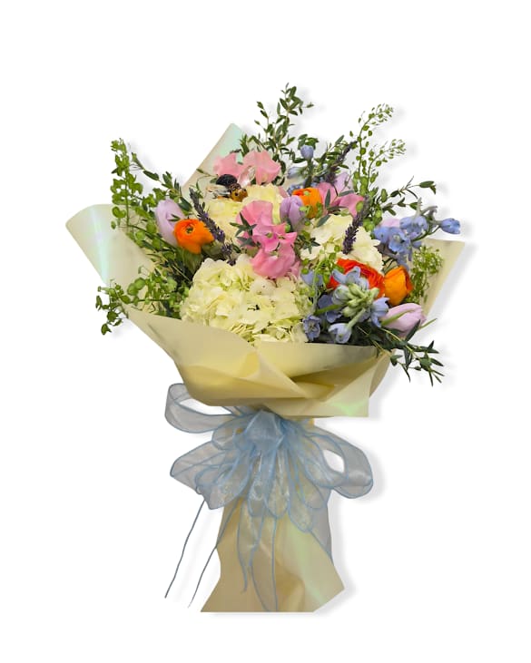Sweet As Can Bee - A vibrant and whimsical wrapped bouquet bursting with playful pops of color and fresh seasonal blooms, designed to make any moment feel special. Finished with a charming keepsake bee stake, this arrangement is wrapped in a wet sponge to keep it fresh for a few hours.   Does not come with a vase.