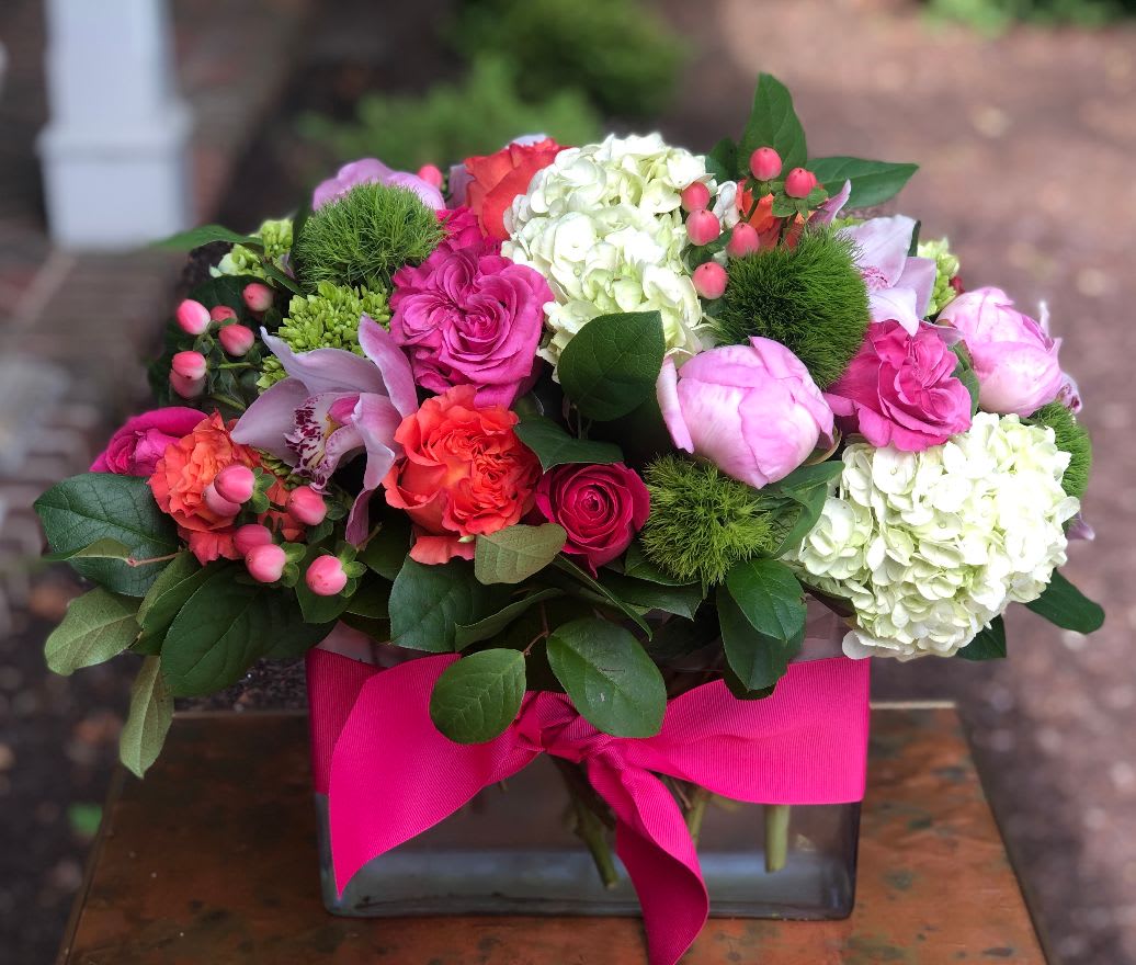 The Westover - The Westover – Colorful Mixed Floral Arrangement | Wilmington, Delaware Local Florist  Brighten any occasion with The Westover, a vibrant floral arrangement expertly crafted by your trusted Wilmington, Delaware florist. This beautiful bouquet features lush white and green hydrangea, rich dark pink roses, bright orange roses, delicate pink hypericum berries, and fresh green trichilium. Presented in a clear glass vase and finished with a striking hot pink ribbon, this arrangement adds a lively pop of color and elegance to any space.  Perfect for birthdays, anniversaries, celebrations, or just because. Available for same-day flower delivery in Wilmington, DE and surrounding areas. Trust our local flower shop for premium, fresh blooms and exceptional customer service.