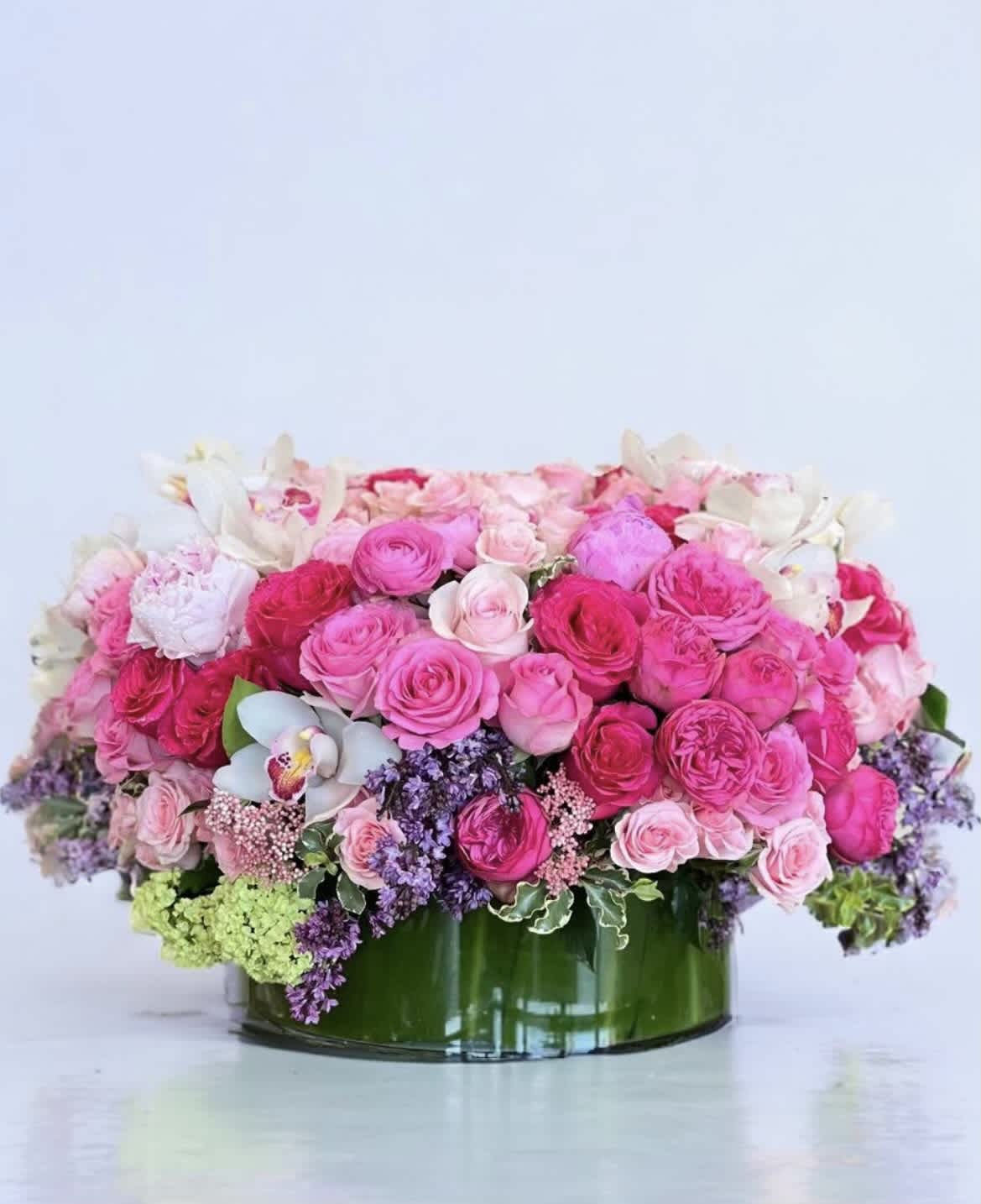 Mother's Grace - A low, tight arrangement showcasing an assortment of pink Roses and other select blooms