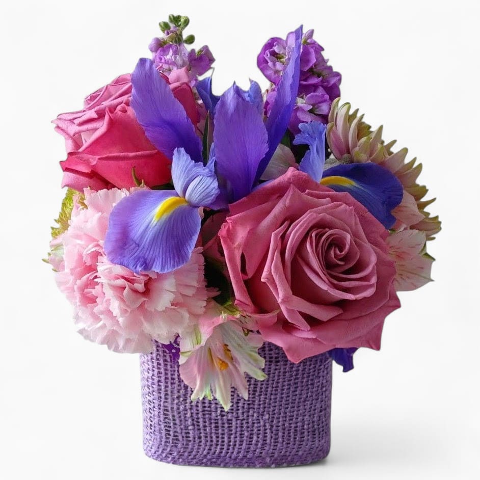 Designer's Choice Purple Cutie - Pretty purple blossoms of the day roses and more arranged in a modern glass vase wrapped in lavender jute ribbon. Send happiness.