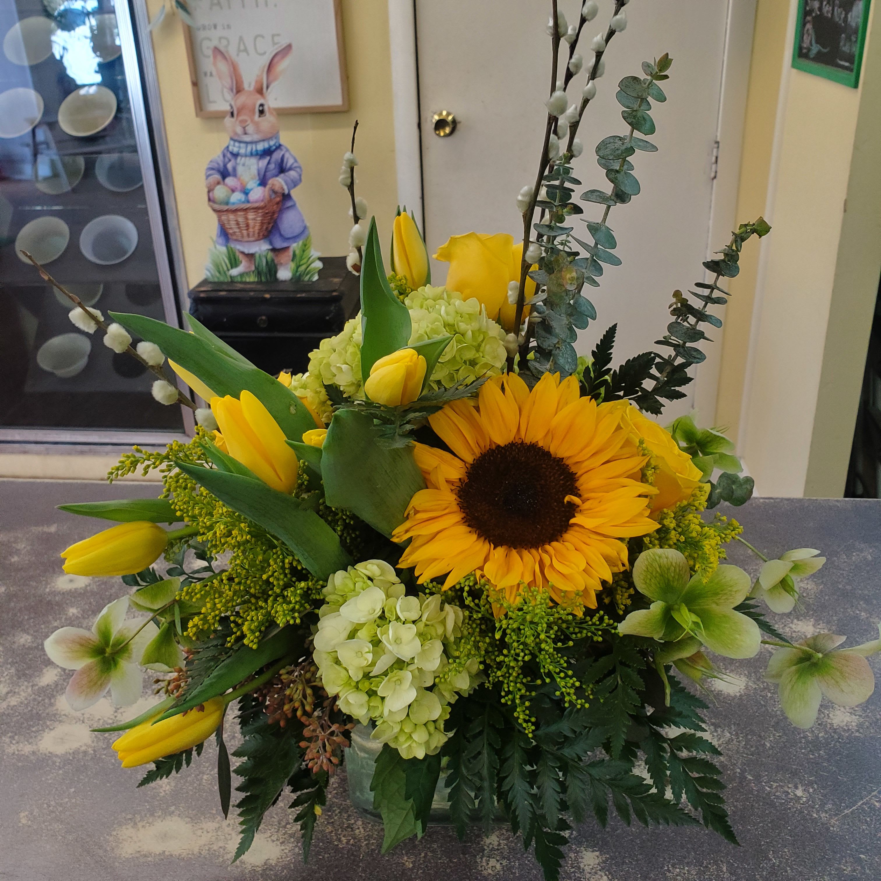 Simply Yellow  - A glass  vase arrangement filled with green hydrangeas, yellow tulips, sunflowers and accented with yellow roses and assorted greens.  **Tight compact design **