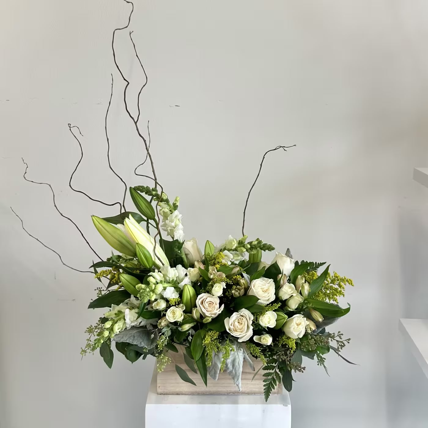 Always Adored - The Always Adored sympathy flower arrangement is a serene, all-white tribute designed to convey eternal love, peace, and heartfelt condolences during times of loss. This elegant sympathy arrangement features pristine white lilies for purity and restoration, classic white roses symbolizing reverence and everlasting affection, delicate white spray roses adding soft texture and fullness, graceful white alstroemerias for enduring devotion, and tall white snapdragons bringing height and gentle elegance. Lush accents of dusty miller provide silvery, velvety contrast, while dramatic curly willow branches add artistic movement and natural sophistication. Complementary greenery enhances the fresh, harmonious composition, creating a timeless display of comfort and remembrance. Perfect for funeral services, memorial visitations, or as a comforting sympathy gift delivered to the home, this pure white floral arrangement offers solace and beauty in grief. Handcrafted with premium fresh flowers, the Always Adored arrangement stands as a dignified expression of sympathy—honoring cherished memories with grace and tranquility. Send condolences that speak volumes with this exquisite all-white sympathy bouquet, a touching gesture of support that families will treasure. Ideal keywords: white sympathy flowers, all white funeral arrangement, lilies and roses sympathy, peaceful condolence flowers, elegant memorial tribute.
