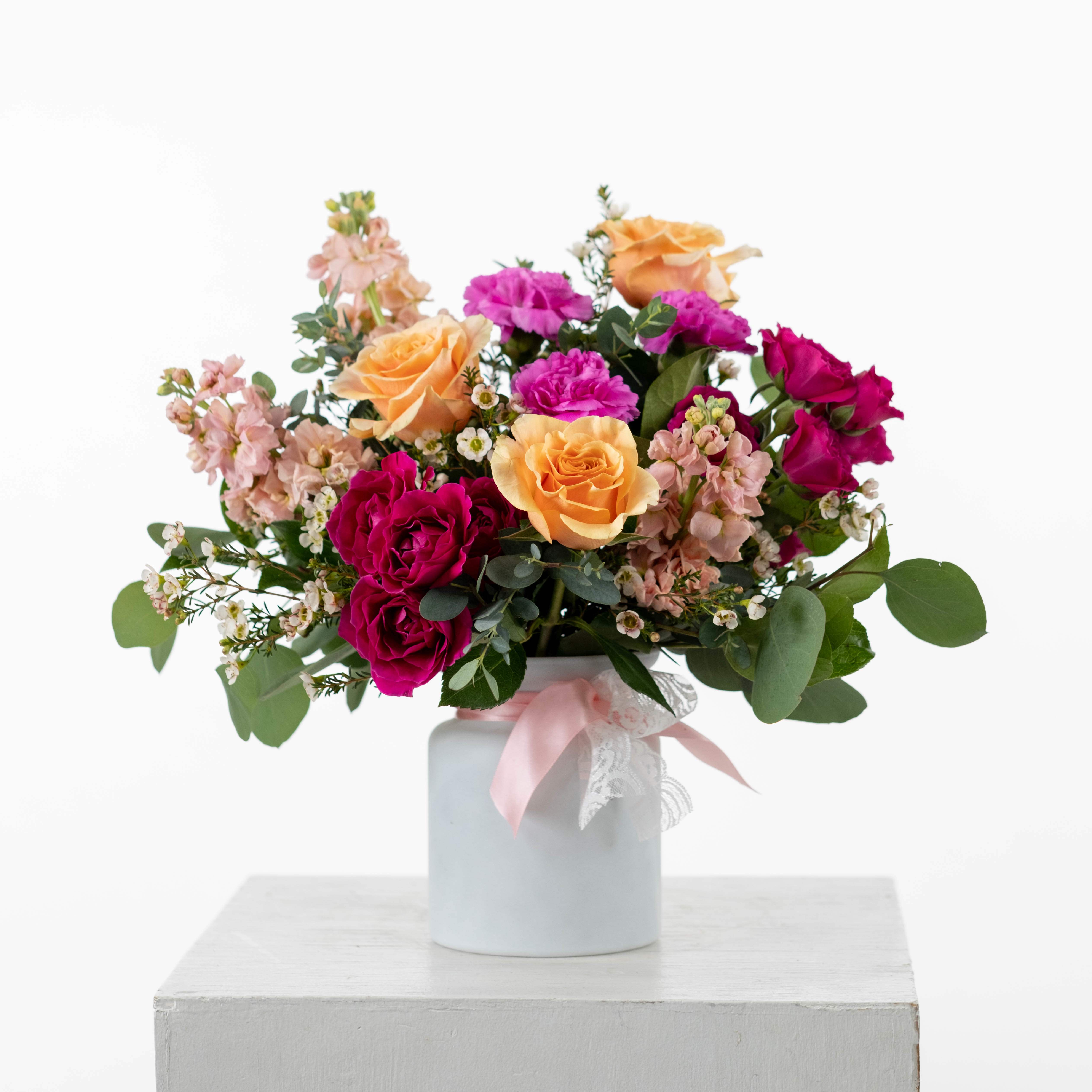 P.S. I Love You - Get ready to swoon with our P.S. I Love You Floral Design – a playful blend blooms that will have hearts aflutter. Nestled in a chic white vase with a peach and lace ribbon, this arrangement is the perfect gesture in the most fabulous and colorful way!  OTHER STYLES AVAILABLE - Please add your preferred style to the special instructions. If there is no preference, the Traditional Style will be chosen for you.  Traditional Style - Peaches and Vibrant Pinks in a White Vase Valentine's Day Style - Reds, Whites, and Pinks in a Red Vase Sweet Love Style - Soft Pinks in a White Vase