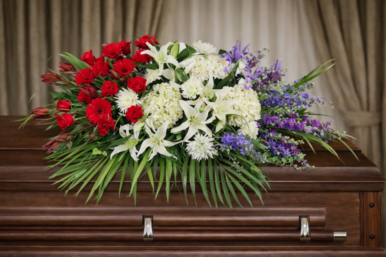 Unity Casket Spray  - The Unity Casket Spray from FloralFabulous is a powerful and meaningful tribute designed to honor a life of love, service, and remembrance. This patriotic funeral arrangement features rich red roses, elegant white lilies, lush hydrangea, and vibrant blue delphinium, beautifully arranged with flowing greenery.  The red, white, and blue color palette symbolizes honor, respect, and remembrance, making this arrangement especially meaningful for celebrating the life of a loved one, including veterans and those who served. Designed to rest gracefully atop the casket, this spray creates a striking focal point during funeral and memorial services.  The Unity Casket Spray offers a beautiful expression of sympathy while reflecting strength, dignity, and cherished memories. Its balanced design and rich colors provide comfort and support to family and friends during a difficult time.  FloralFabulous proudly provides funeral flower delivery and patriotic sympathy arrangements in Round Rock, TX and the greater Austin area, helping families express love, remembrance, and heartfelt support..