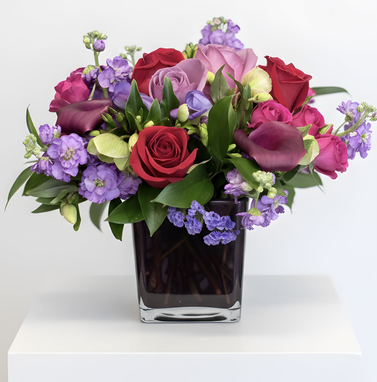 Bejeweled Beauty - Pure romance. Hot pink roses and dark red spray roses are brightly arranged inside our violet cube.  Hot pink roses, dark red spray roses, purple calla Lily are accented with assorted greens