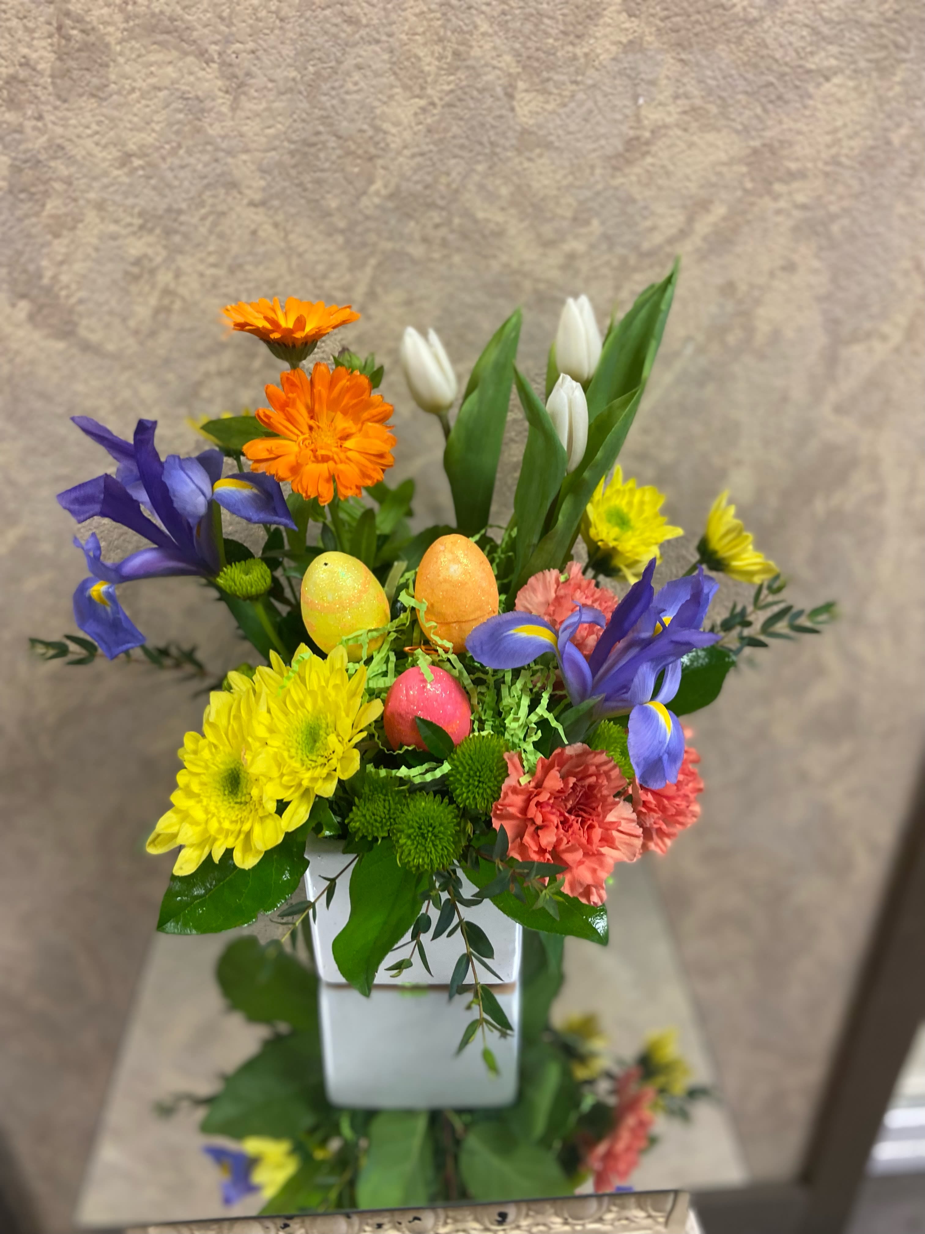 Spring Delight - Recipes: Blue Iris, Orange Calendula, White Tulips, Coral Carnations, Yellow Daisies and Green Buttons in a short, white vase. Availability: Calendula- early Spring to Fall Substitute Available: Yes Design View: Symmetric Front Facing View Photo shown: Regular 