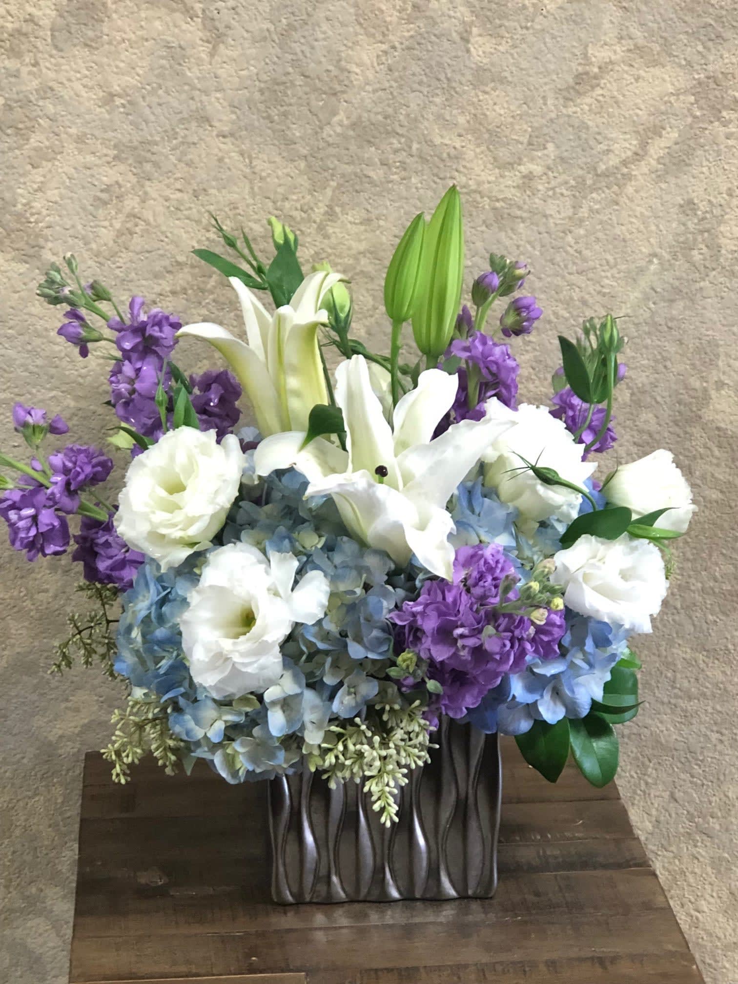 Moon River - Type of Flowers: White Snapdragon, White oriental Lilli, Lavender Stock, and Blue Hydrangeas in a silver, short vase. Availability: All year round Substitute Available: Yes Design View: Symmetric Front Facing View Photo shown: Regular