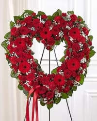 Heart of Remembrance Spray - A striking all-red standing spray arranged in an open heart design, symbolizing love, honor, and remembrance. This florist’s choice arrangement allows for seasonal or available blooms, ensuring a fresh and beautiful display, though specific flowers may vary from the image. Lush greens complement the vibrant red tones, creating a bold and heartfelt tribute.