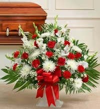 Crimson &amp; White Comfort Basket - A graceful sympathy floral basket featuring a classic blend of white cushion mums, white spider mums, red carnations, and a red rose, beautifully complemented with white asters, jade foliage, and fresh greenery for a full and balanced display.  Finished with a red ribbon bow, this elegant arrangement combines the purity of white blooms with the warmth of red accents, symbolizing love, respect, and remembrance. Designed in a traditional basket, it offers a heartfelt expression of sympathy and comfort during a difficult time.