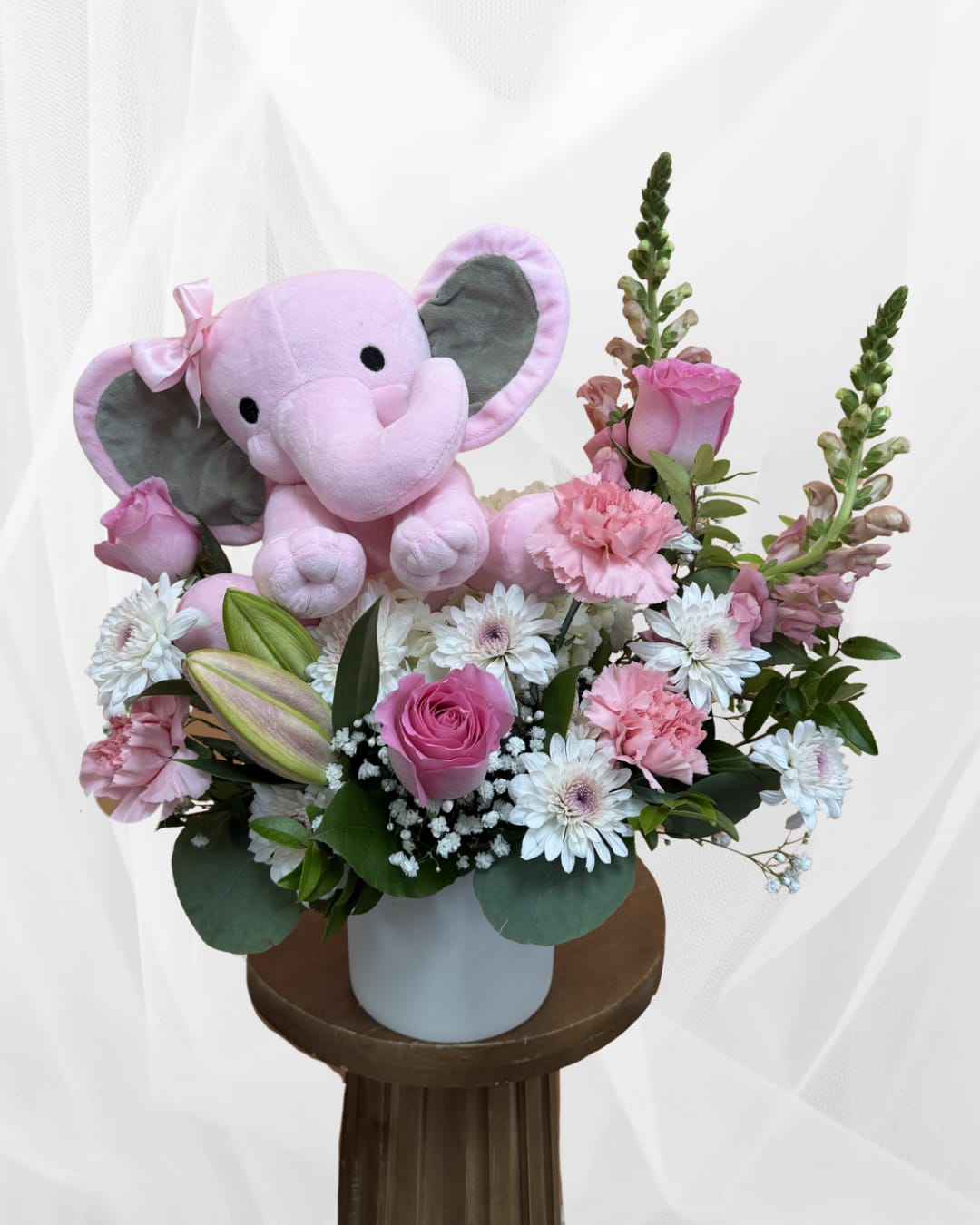Baby Bella's Elephant Garden  - Celebrate the arrival of a sweet baby girl with a beautiful floral arrangement designed to welcome new life with warmth and joy. This design features hydrangea, pink roses, and delicate accent blooms arranged in a keepsake container alongside an adorable plush elephant. Aprox. dimensions 16x16