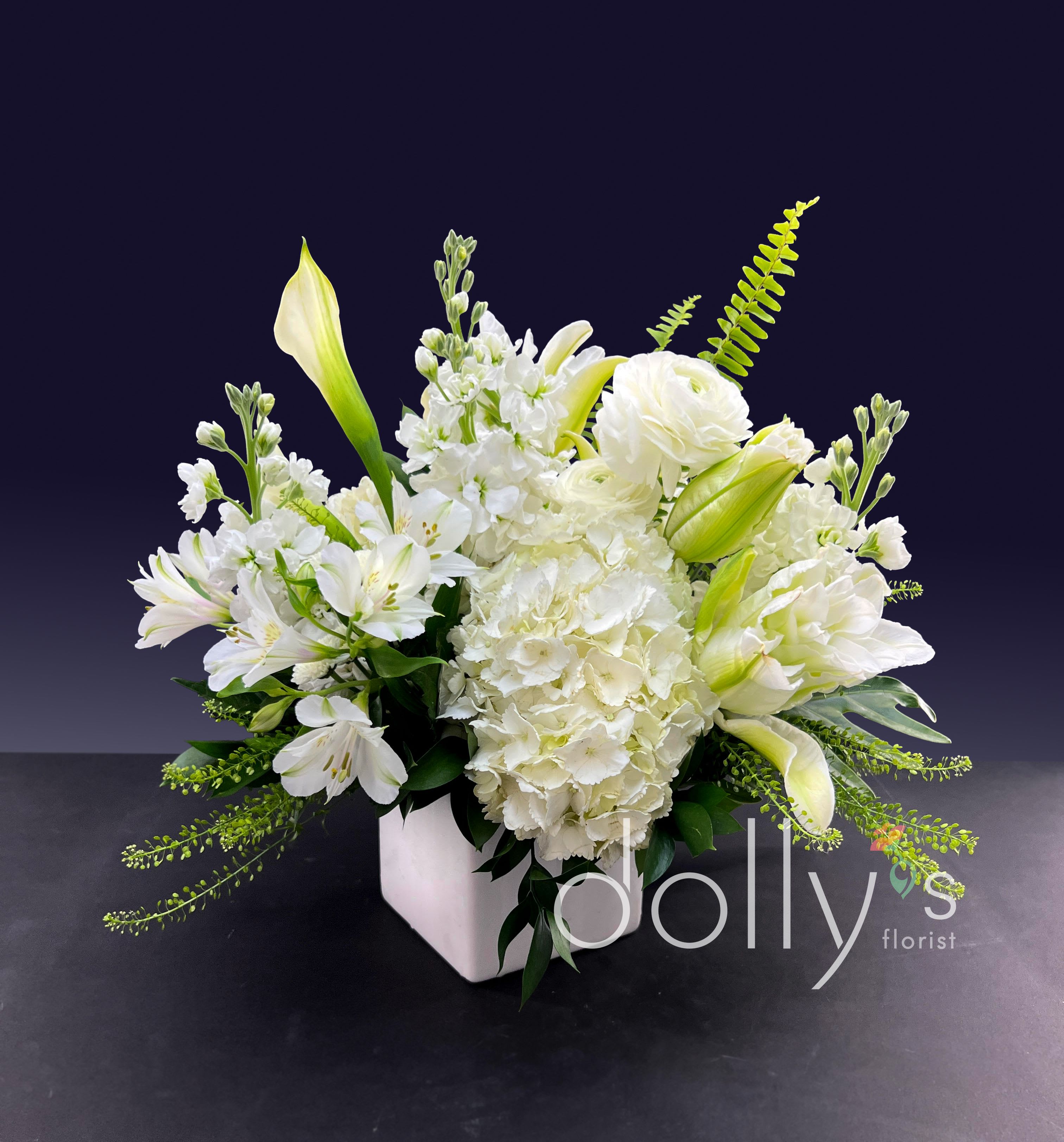 White floral arrangement in a square vase with lilies and hydrangeas