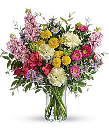 Mixed bouquet of pink, yellow, white, and purple flowers in a glass vase