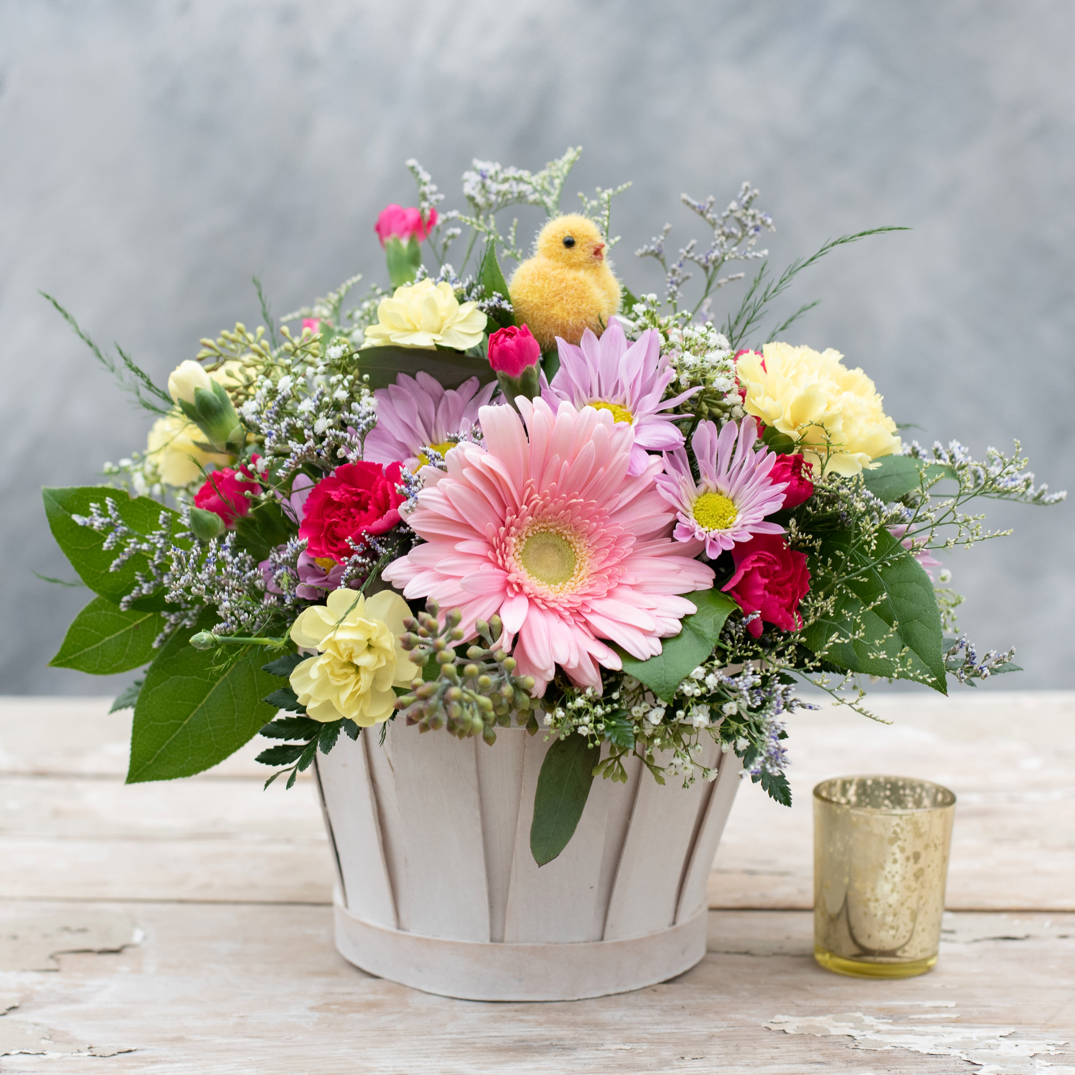Easter Basket - Pretty and bright white colored basket   filled with colorful spring blooms! A sweet little Easter chick sits atop this arrangement that would be perfect for a table centerpiece or foyer.  