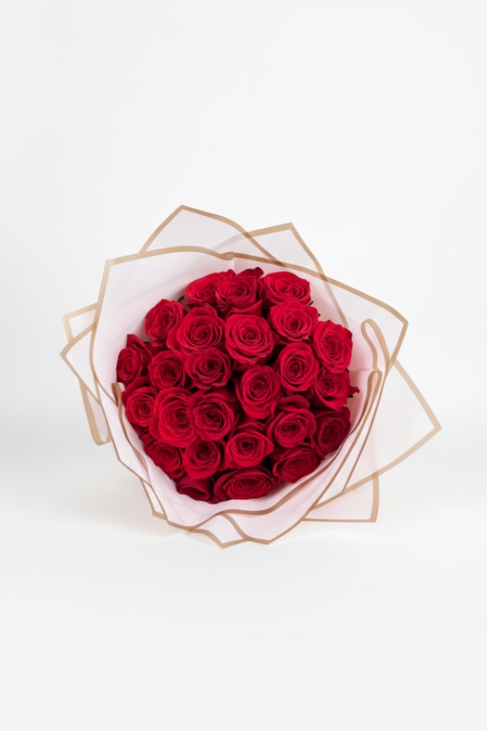 Round bouquet of red roses wrapped in white tissue and tan-edged paper
