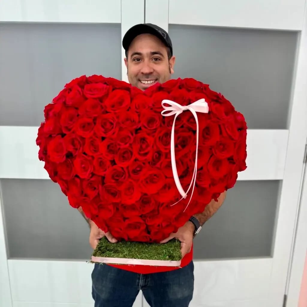 Standing Rose Heart - Make a statement of love with our luxurious handcrafted rose heart — designed to captivate at first glance. This stunning arrangement features approximately 150 of premium roses meticulously placed to form a full, symmetrical heart silhouette. Each bloom is selected for its vibrancy and freshness, creating a lush, velvety texture from edge to edge.  Set atop on a base accented with natural moss, this piece offers a modern yet romantic presentation. A delicate satin ribbon detail adds an elegant finishing touch, making it perfect for gifting or as a show-stopping décor piece.  Perfect for: • Anniversaries • Valentine’s Day • Engagement celebrations • Bridal showers • Luxury romantic gestures  Bold, luxurious, and unforgettable — this rose heart is more than flowers; it’s an experience. 