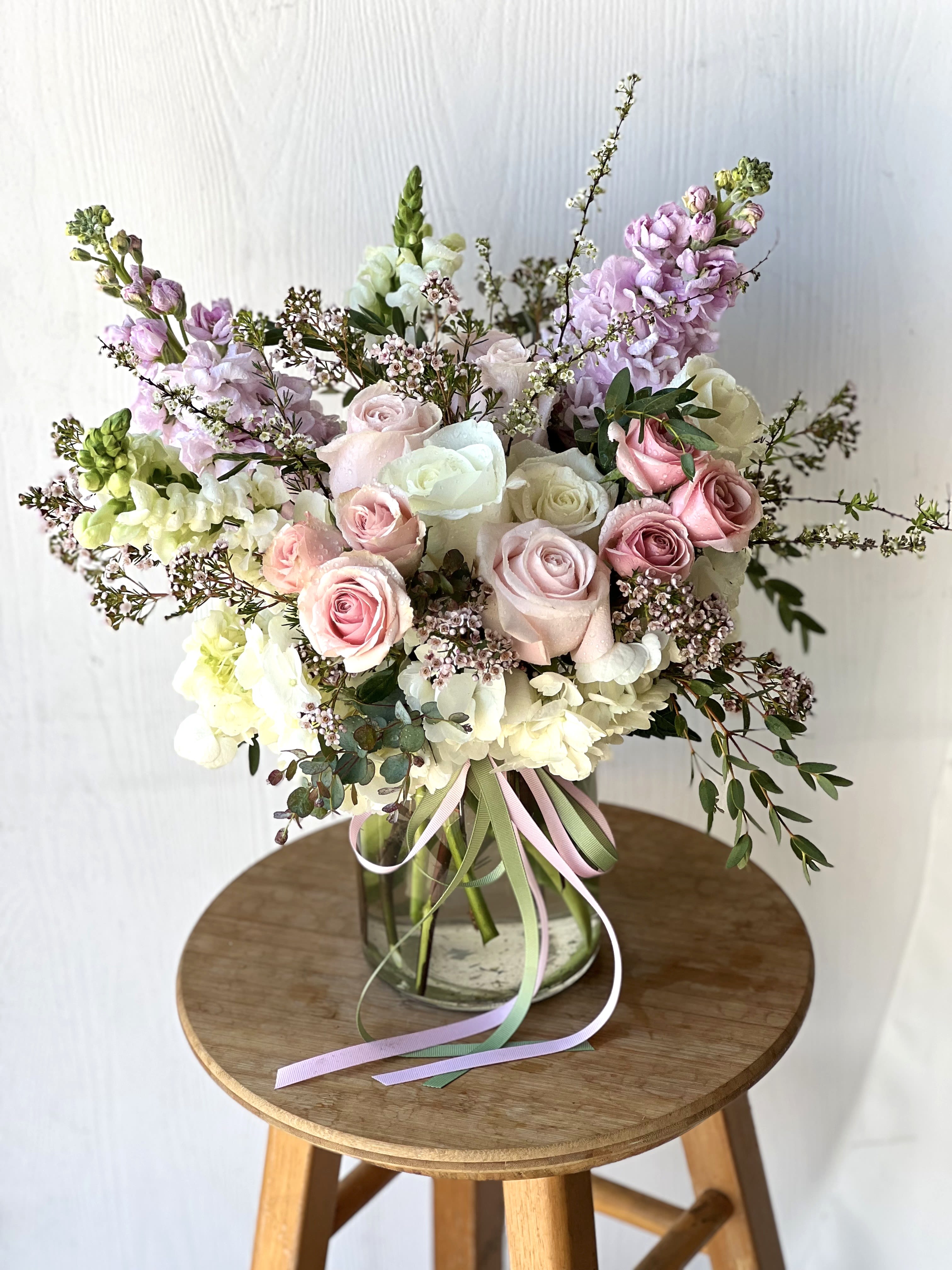 EC81 - Love You More - Tell that special someone that you love them more with this gorgeous arrangement. This arrangement features hydrangea, pink spray roses, roses, wax flower, and Larkspur and is the perfect bouquet of flowers to give for Mother's Day, anniversary, birthday, or just because. This flower arrangement is delivered in a clear glass milk vase.   Size: approx 15" tall, 9" wide