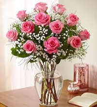Classic Pink Dozen Roses - A classic and elegant arrangement featuring one dozen beautiful pink roses, artfully arranged in a clear glass vase. Accented with fresh greens and complemented by delicate baby’s breath or white asters (based on availability), this timeless design offers a soft and charming presentation perfect for any occasion.