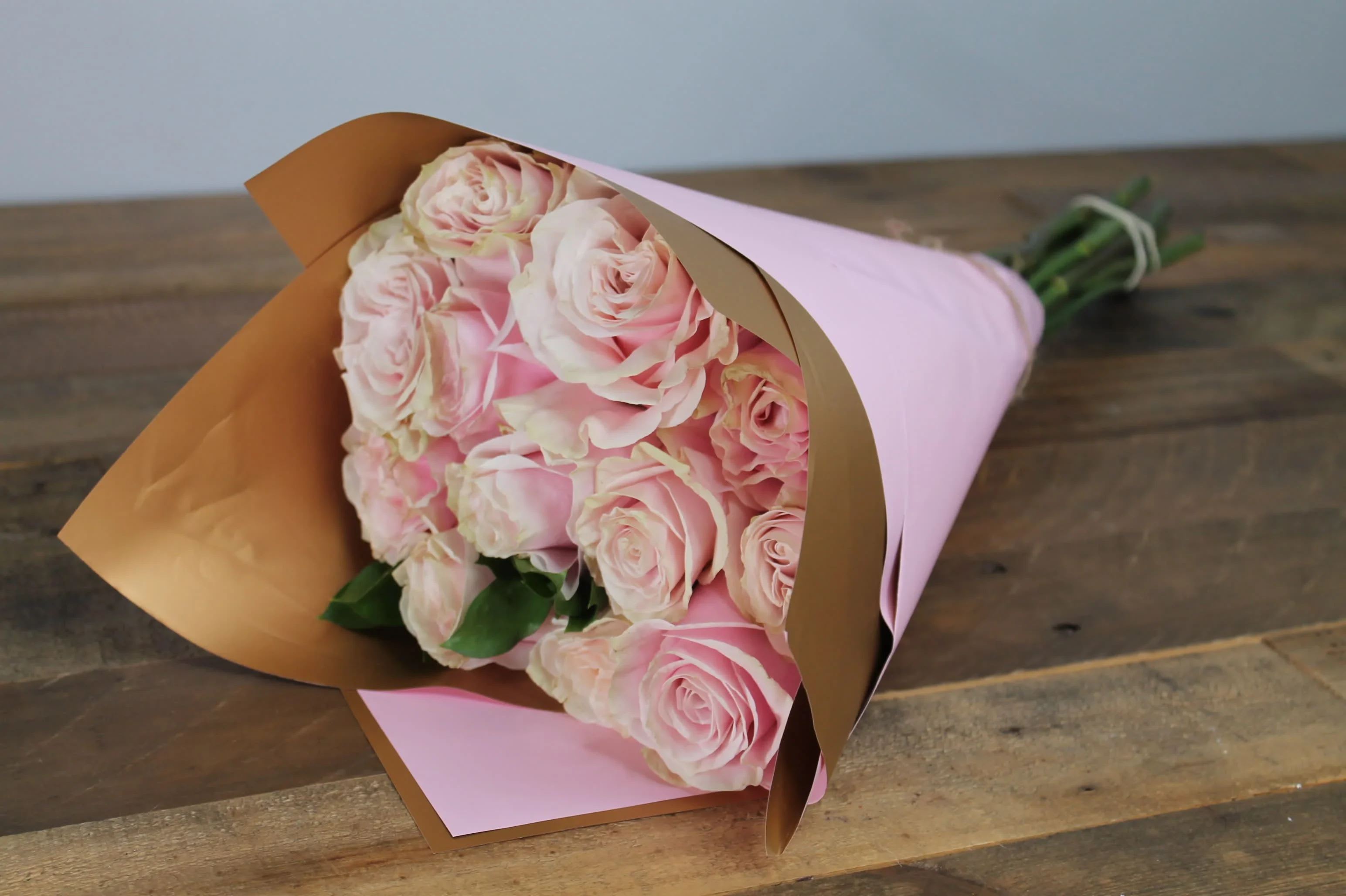 Charming Embrace - Elegant arrangement of a dozen exquisite light pink roses, beautifully presented in waterproof floral wrap to ensure lasting freshness.