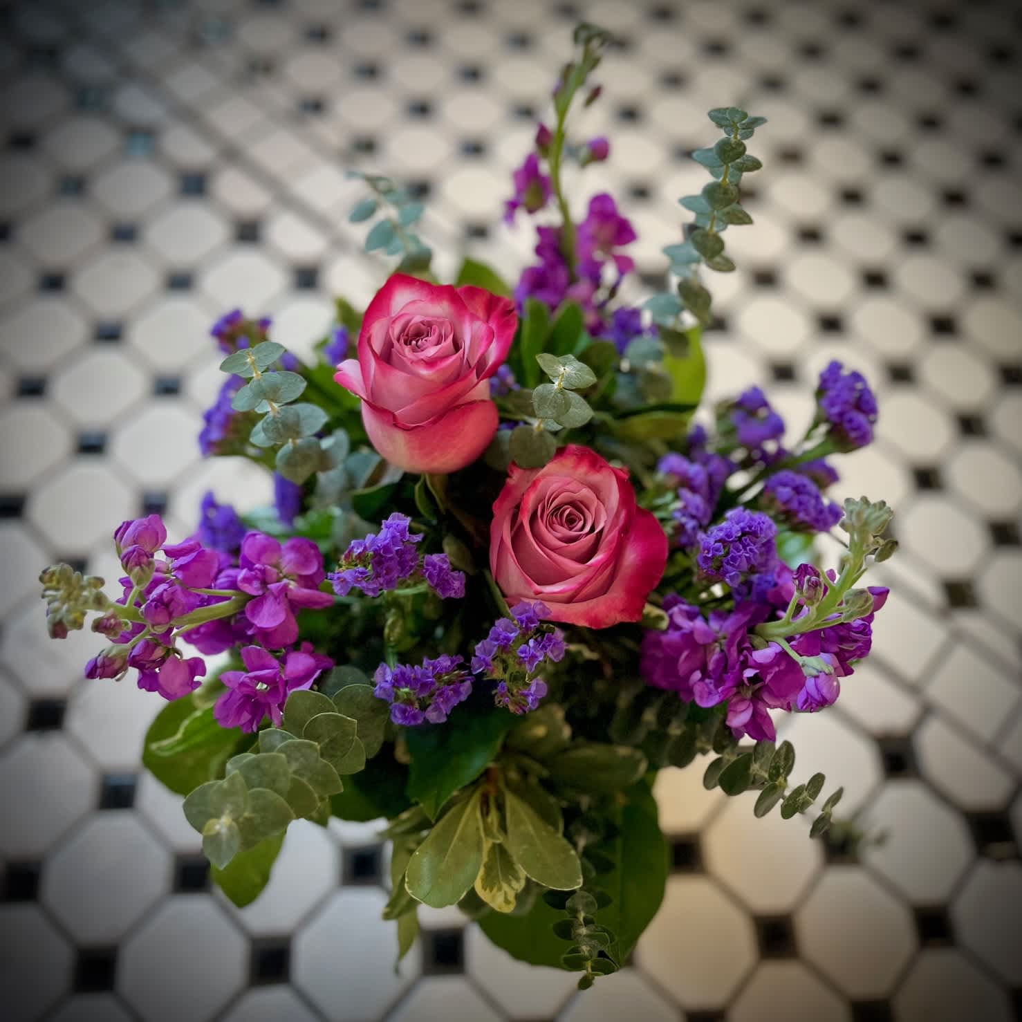 Purple Passion - "Purple Passion" Is a beautiful monochromatic arrangement featuring two purple roses, purple stock, statice and elegant foliage. Display your unique love with this gorgeous design! This arrangement sits approx. 12 inches tall and 10 inches wide. 