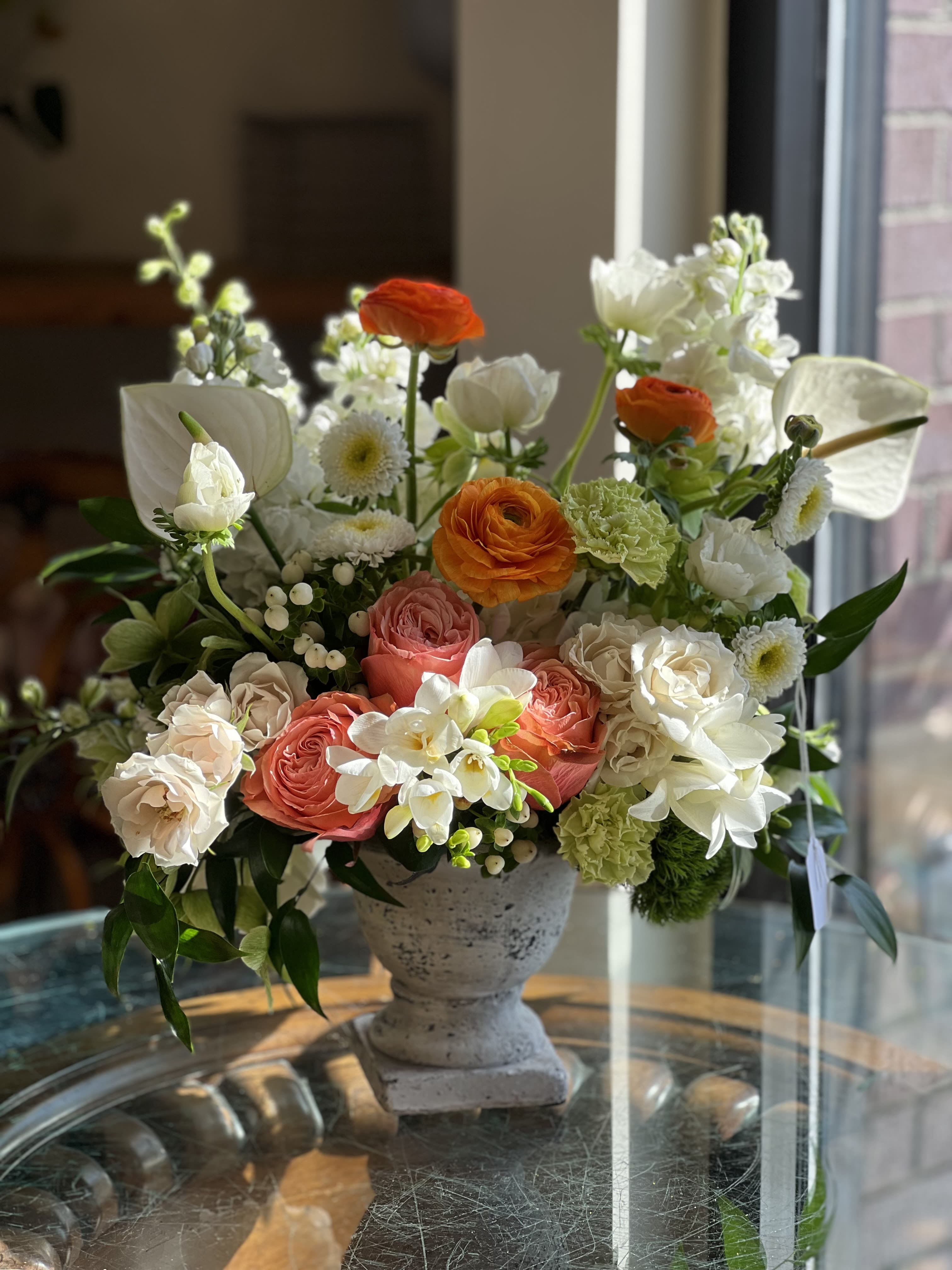 Fresh Summer  - Flowers: coral garden roses, ivory spray roses, white freesia, anemones, white hypericum, white stock, orange ranunculus, white anthurium, dianthus, green carnation, and italian ruscus.   Vase: medium size urn 
