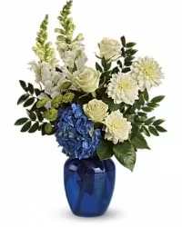 Seaside Harmony - A fresh and vibrant arrangement inspired by the colors of the sea. This seaside-themed display features cheerful mums, elegant roses, green button mums, and striking blue hydrangeas, all accented with lush fresh greens. Arranged in a contemporary blue glass vase, the combination of textures and cool tones creates a refreshing and uplifting presentation perfect for any occasion.