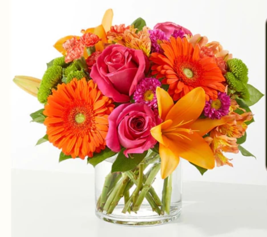 Bright mixed bouquet with pink roses, orange gerberas, and yellow lilies in a glass vase