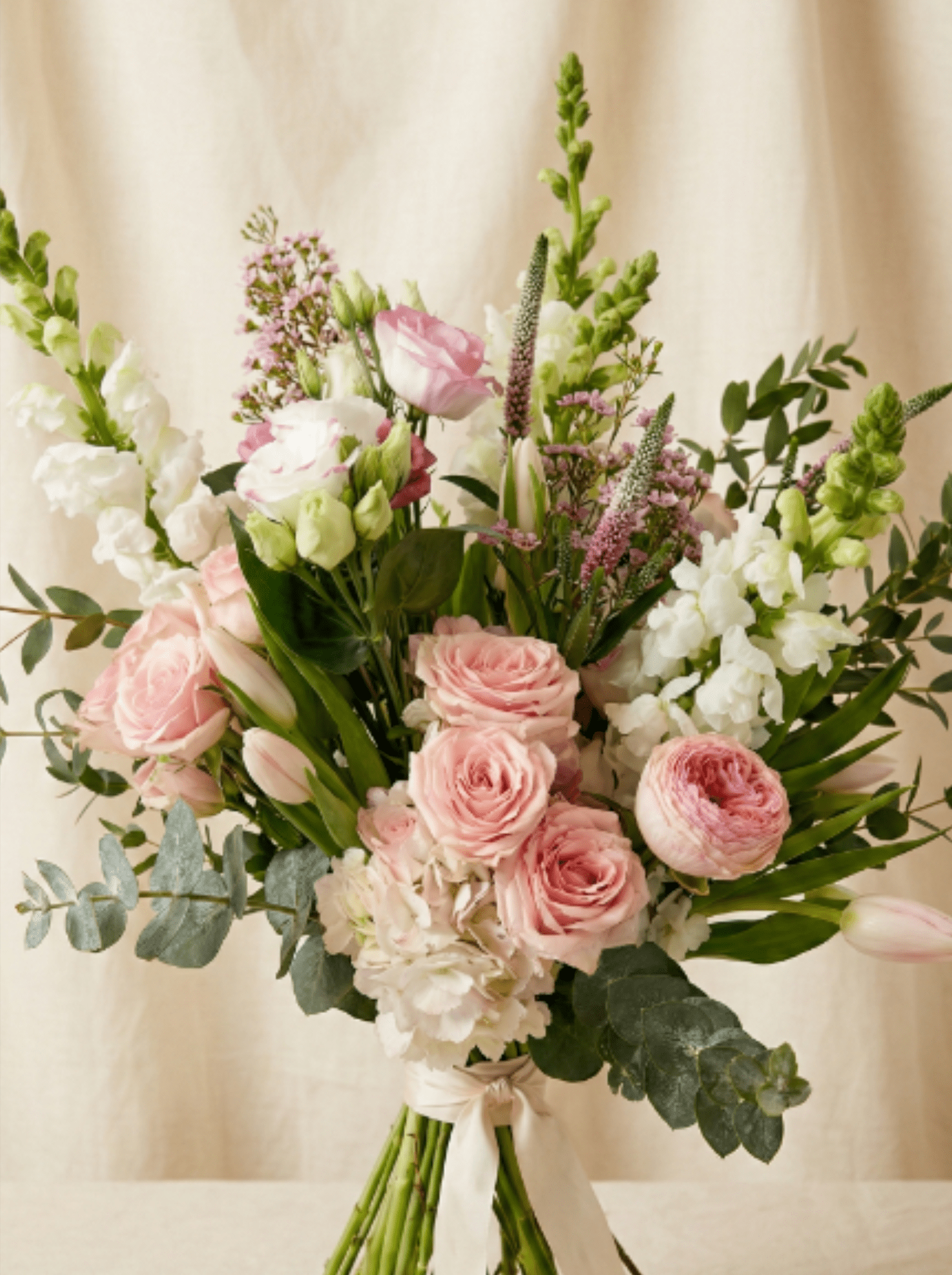 Tall hand-tied bouquet of pale pink roses, tulips, and white flowers tied with a ribbon