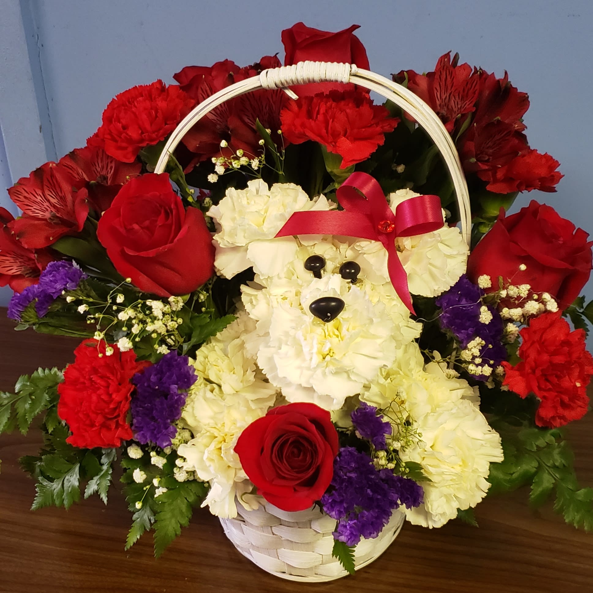 PREMIUM BAYLEE  - A white carnation puppy in a basket full roses and other blooms to celebrate "Your Love"   This is a long lasting arrangement.