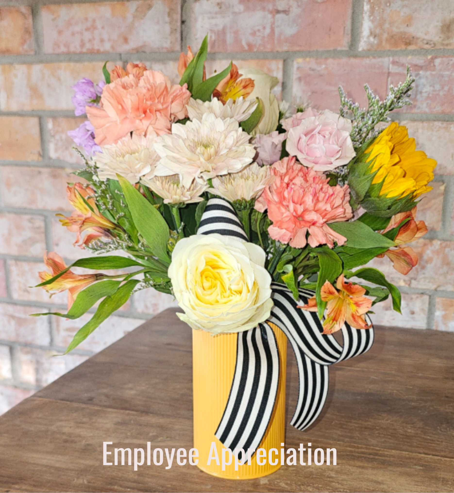 Mixed bouquet in a yellow vase with striped ribbon and pastel flowers including a yellow rose and sunflower