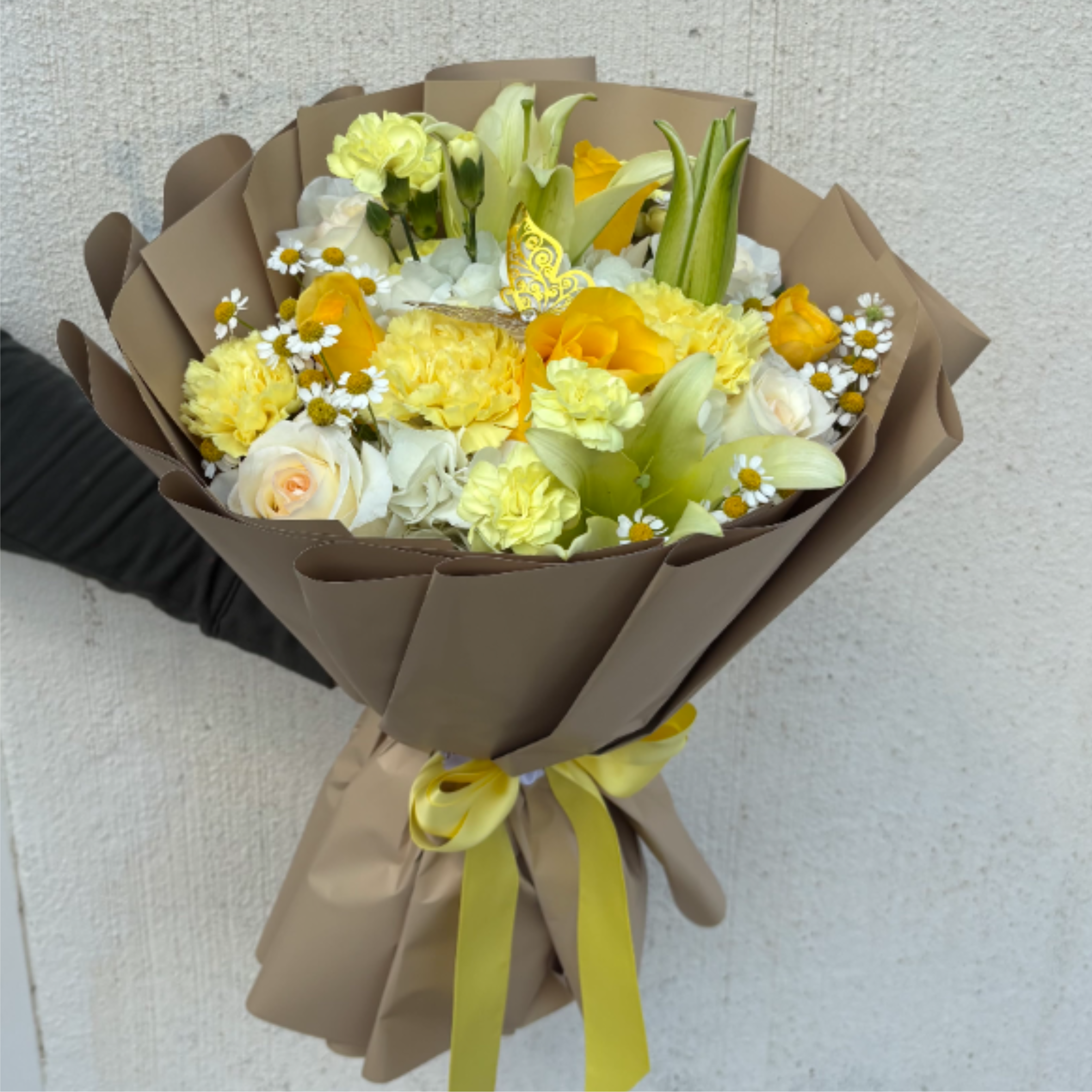 Hand-tied bouquet of yellow and white flowers wrapped in tan paper with a yellow ribbon