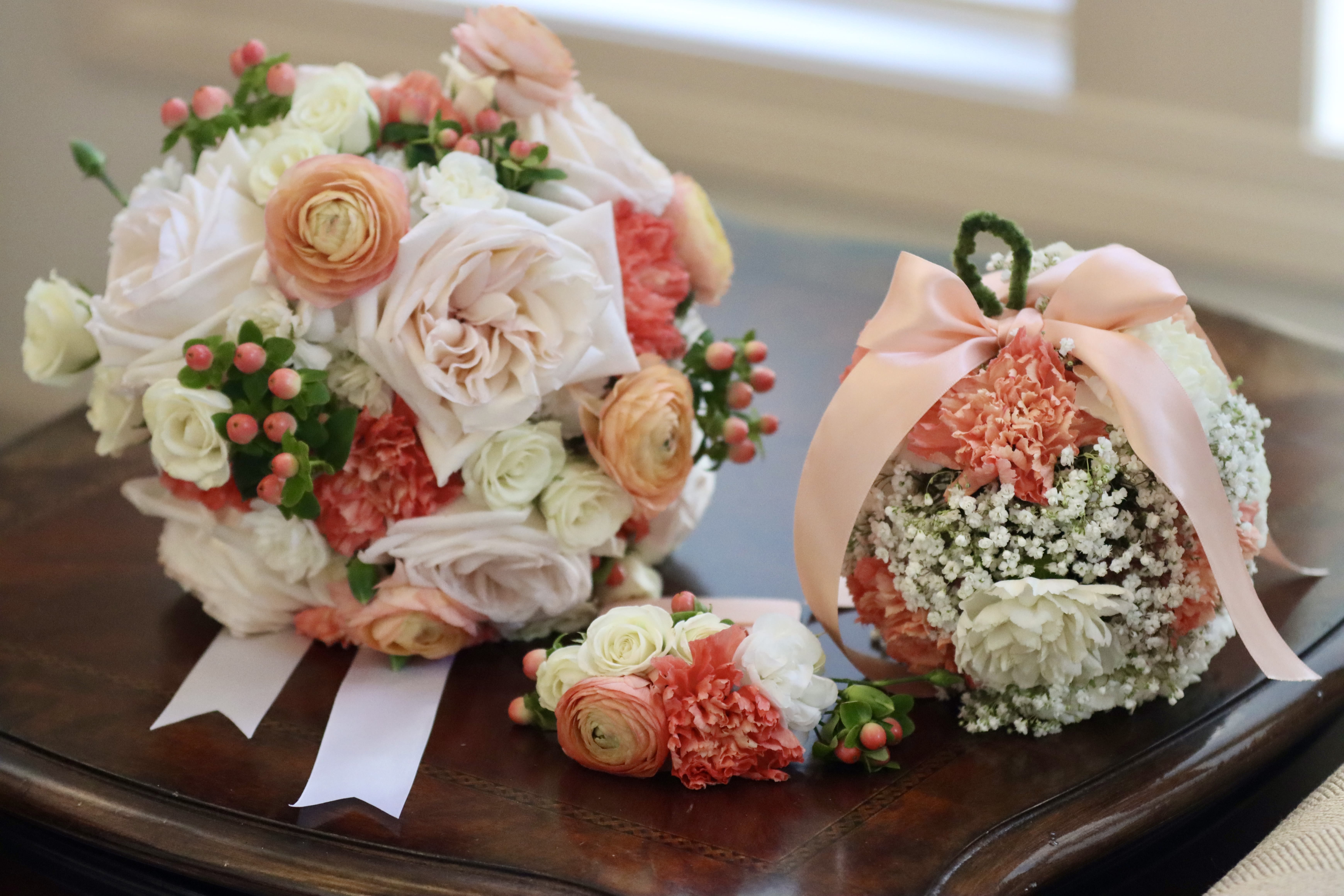  Coordinated Bridal Set: Bouquet, Boutonniere &amp; Pomander - Complete your bridal look with this elegant set, featuring a beautifully coordinated bouquet, pocket boutonniere, and pomander. The soft peach and cream tones of roses, ranunculus, carnations, and baby’s breath are accented with delicate greenery and finished with a charming pink ribbon. Perfect for adding a cohesive and romantic touch to your wedding day, this set is ideal for bridesmaids, flower girls, and the bride herself.